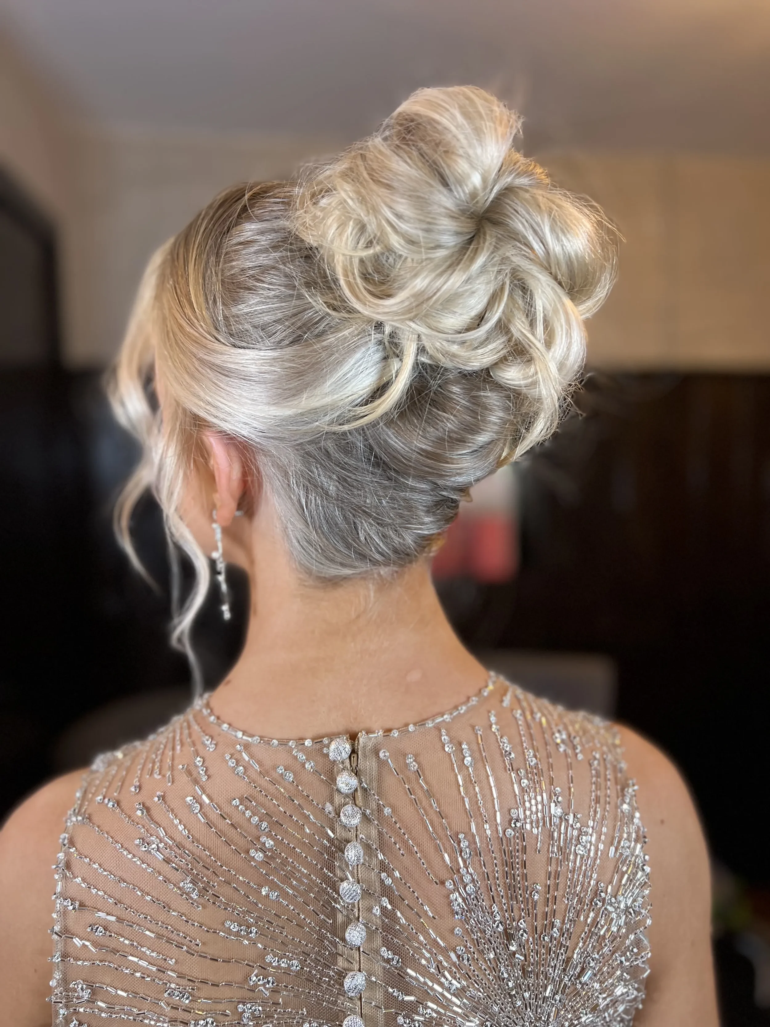Close-up of an elegant bridal updo hairstyle with blonde hair, worn with a sparkling gown embellished with rhinestones and beads.