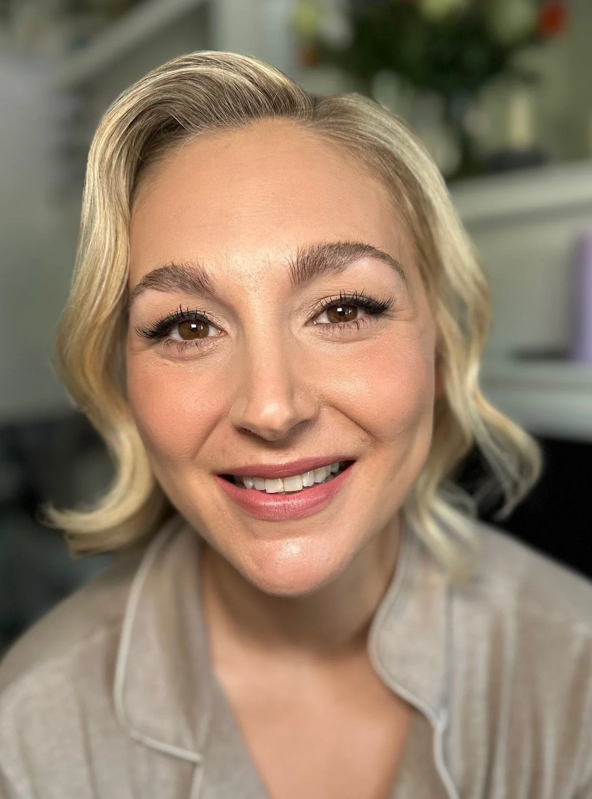 Close-up portrait of a smiling woman with blonde wavy hair, wearing naturally enhancing wedding makeup.