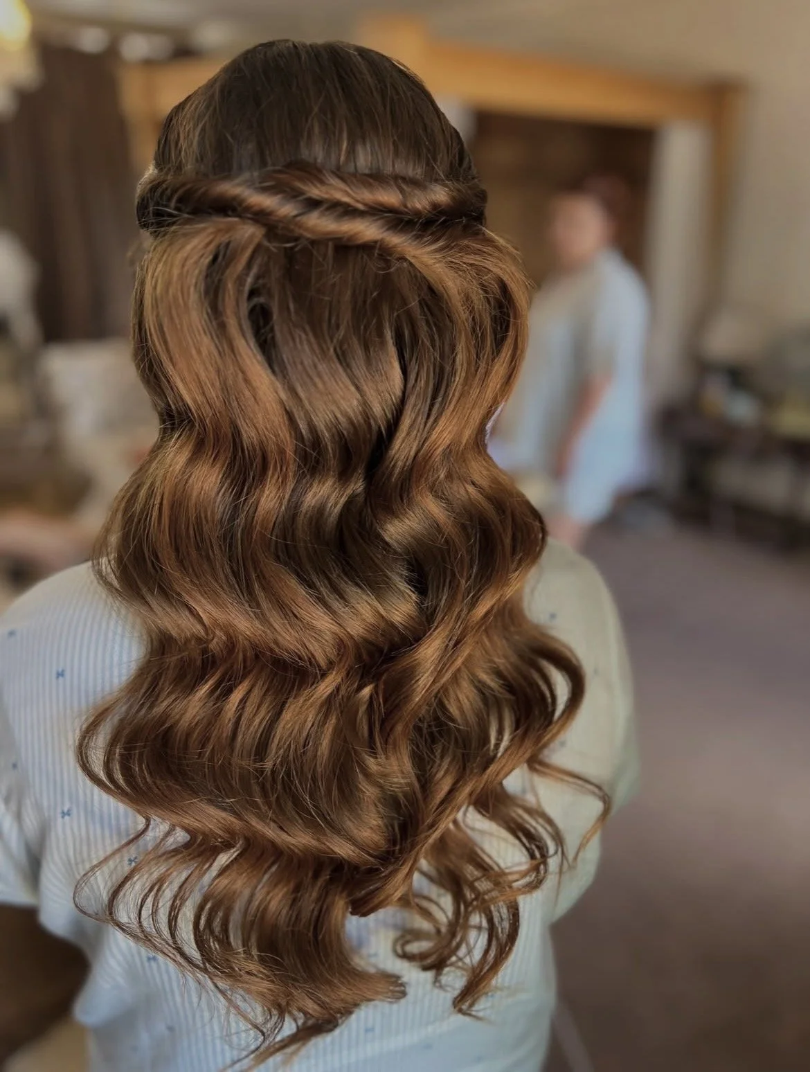Back view of a woman with long, wavy, auburn hair styled with soft waves and twists.
