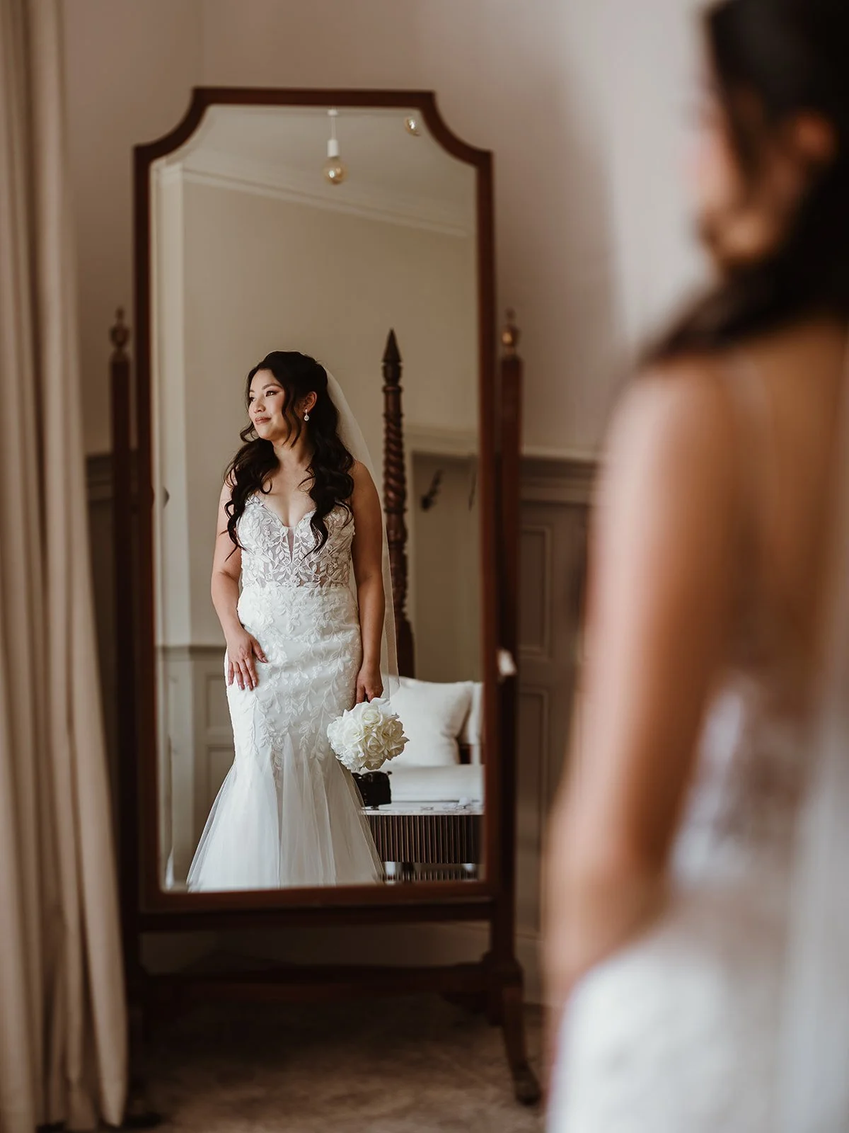 bride on her wedding day, standing in front of a mirror,  holding her bouquet