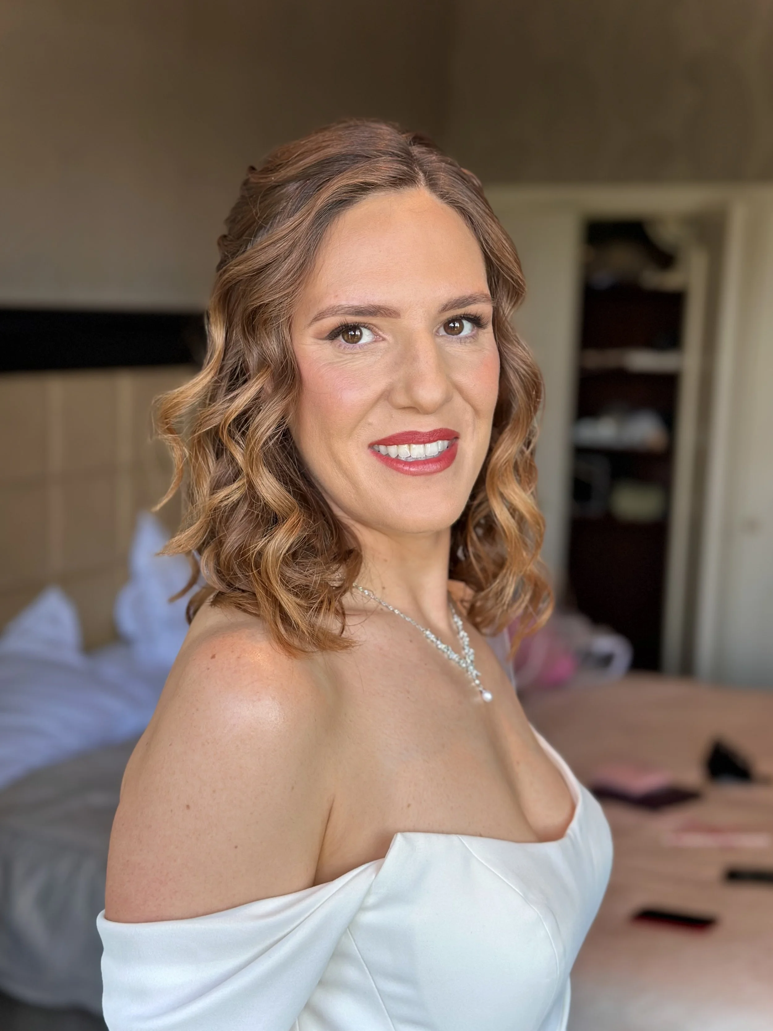 Bride on her wedding day smiling at the camera, wearing natural makeup and a bold red lip.