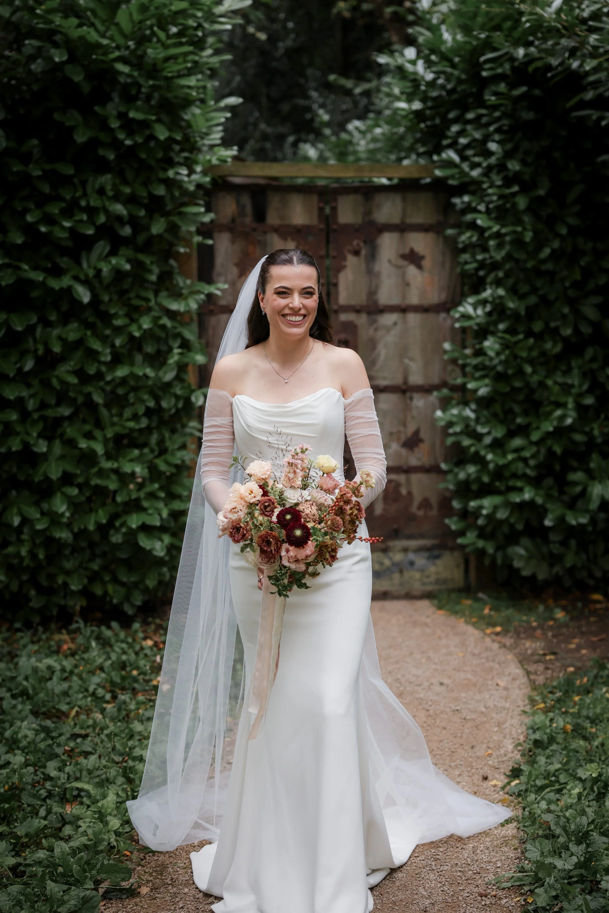 Image of a bride wearing a white wedding dress and holding a bouquet, standing outside