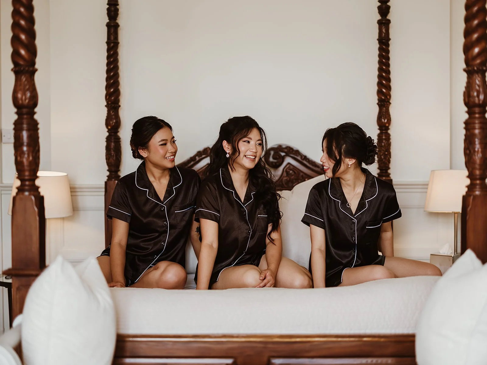 Bride and her bridal party sitting on a bed in the bridal suite at Highley Manor wedding venue