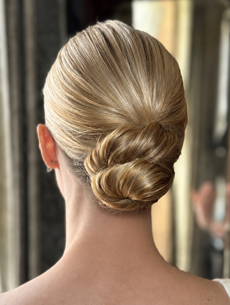 Back of a woman's head with blonde hair styled in a smooth, shiny, elegant bun.