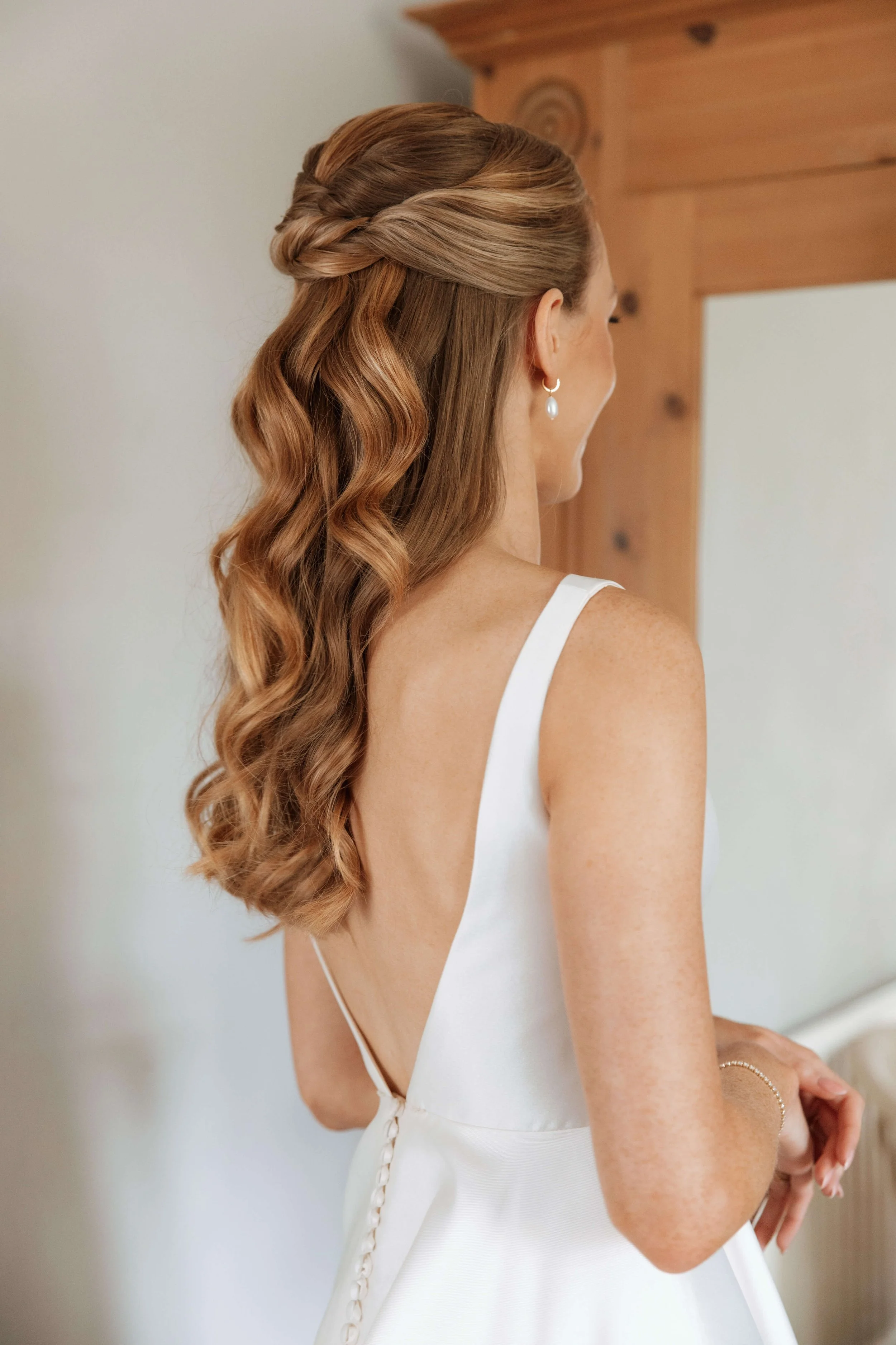 Image of a bride showing the back and side view of her hair, which is styled with soft waves in a half-up half-down style.