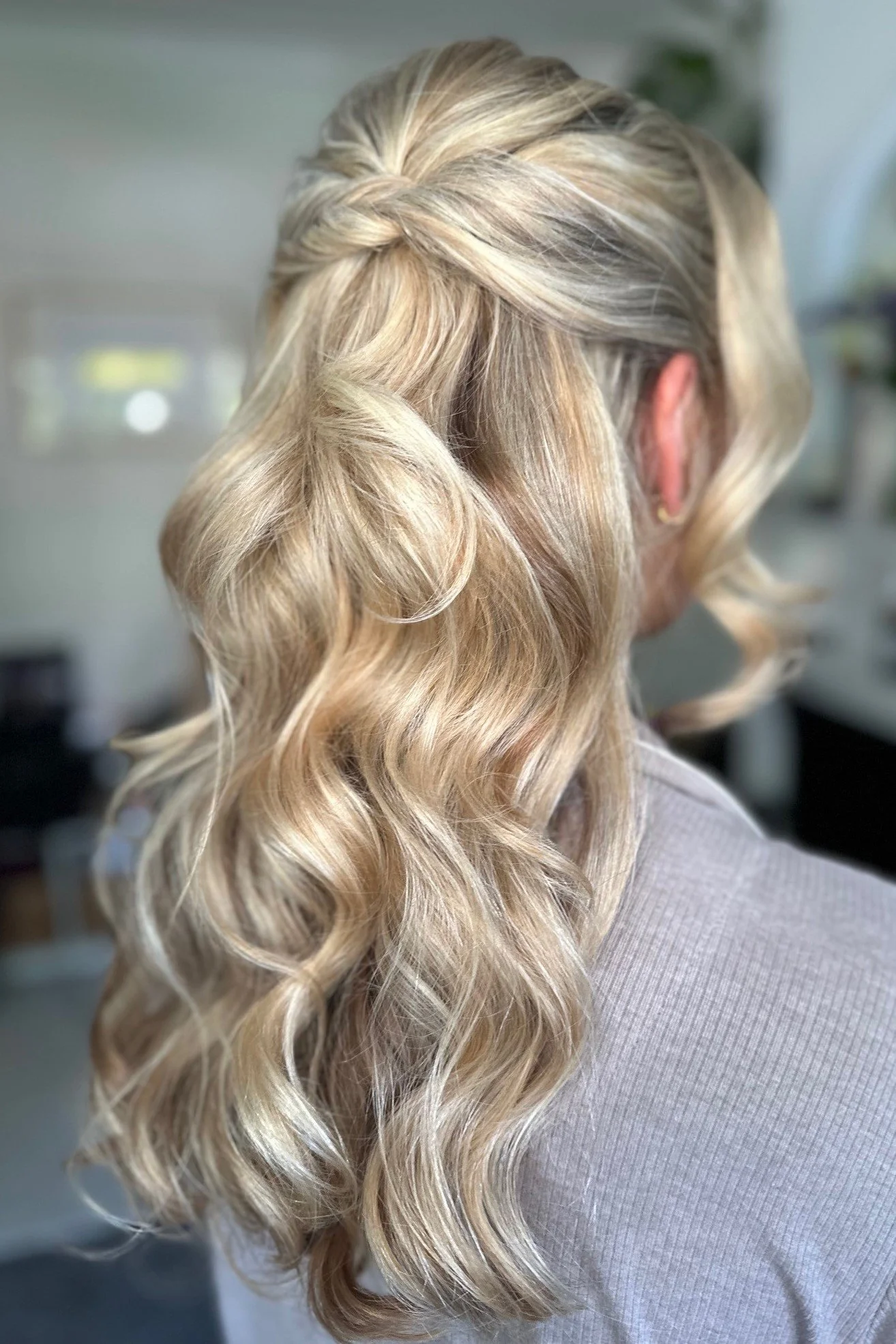 Bridal hairstyle showing long, wavy blonde hair styled in a loose curl and a twisted detail at the crown.