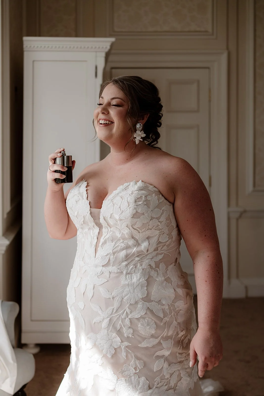 a bride on her wedding day, wearing a white wedding dress and spraying herself with perfume