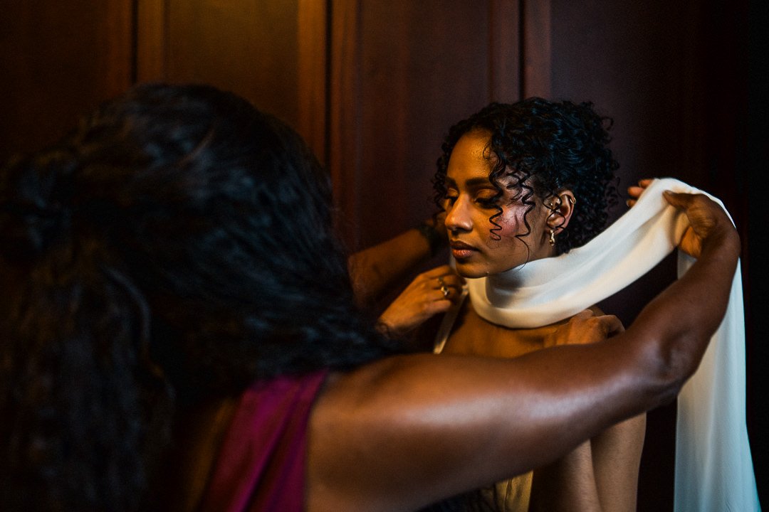A bride on her wedding morning being dressed, wearing soft glam makeup and curly hair undo