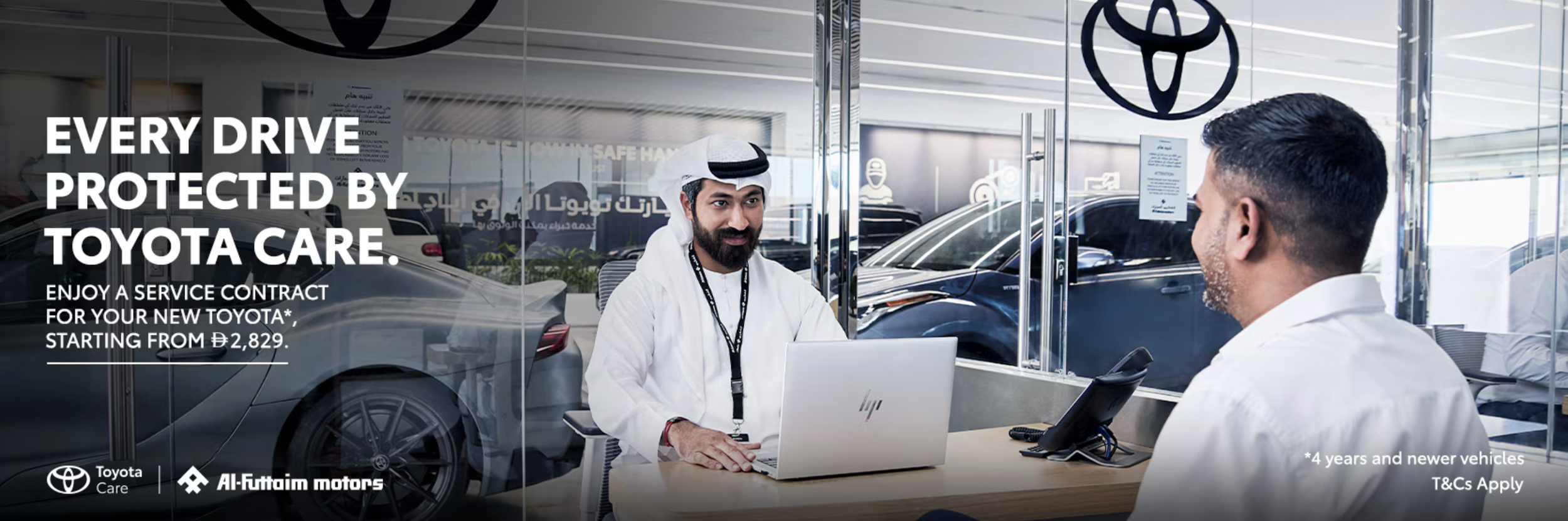 A sales representative in traditional Middle Eastern attire assisting a customer at a Toyota dealership, with cars visible through glass windows.
