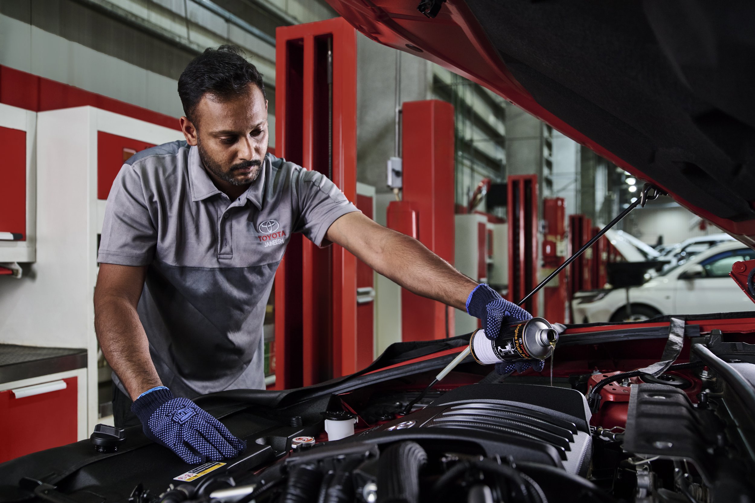 Automobile mechanic working under the open hood of a car at an automotive repair shop.