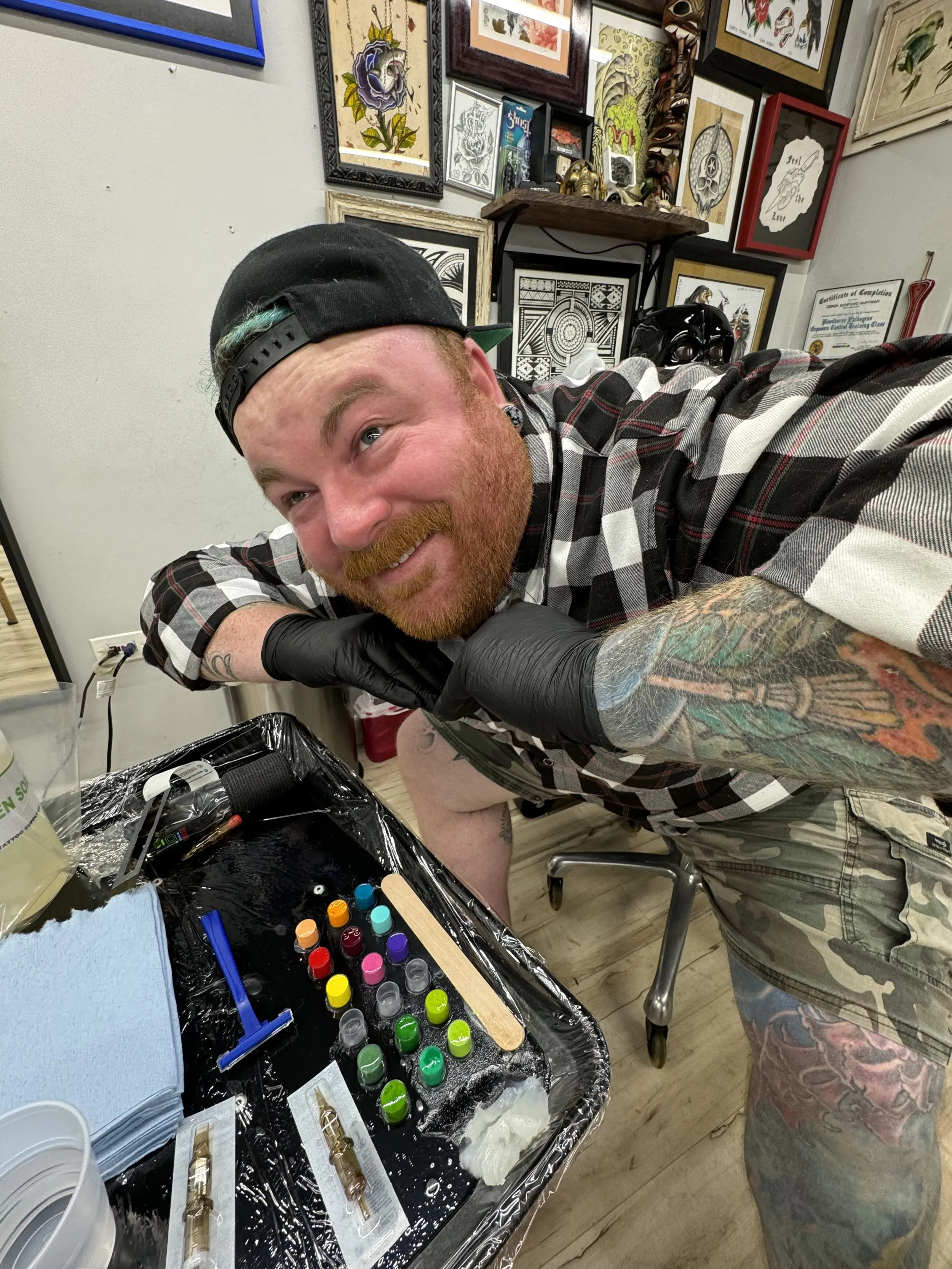 A tattoo artist working on a person's thigh tattoo, surrounded by various tools and supplies in a tattoo studio.