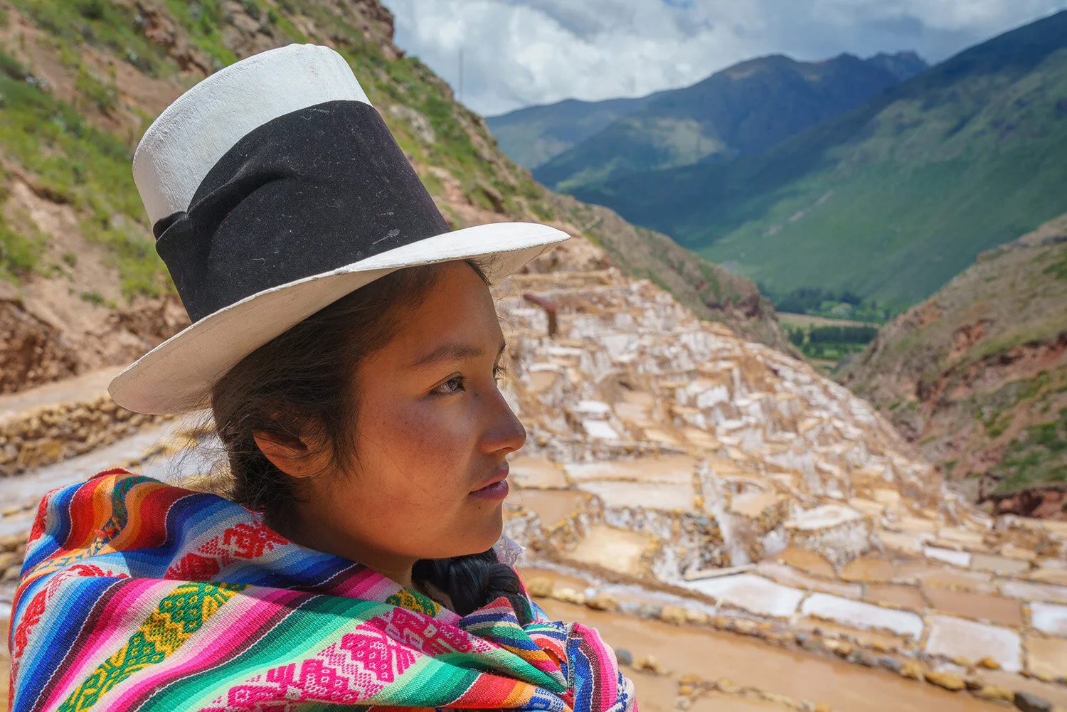  Quechua Mesbize (mixed race signified by white hat) woman  in Salinaras District of Maras overlooking salt ponds in Peru. 