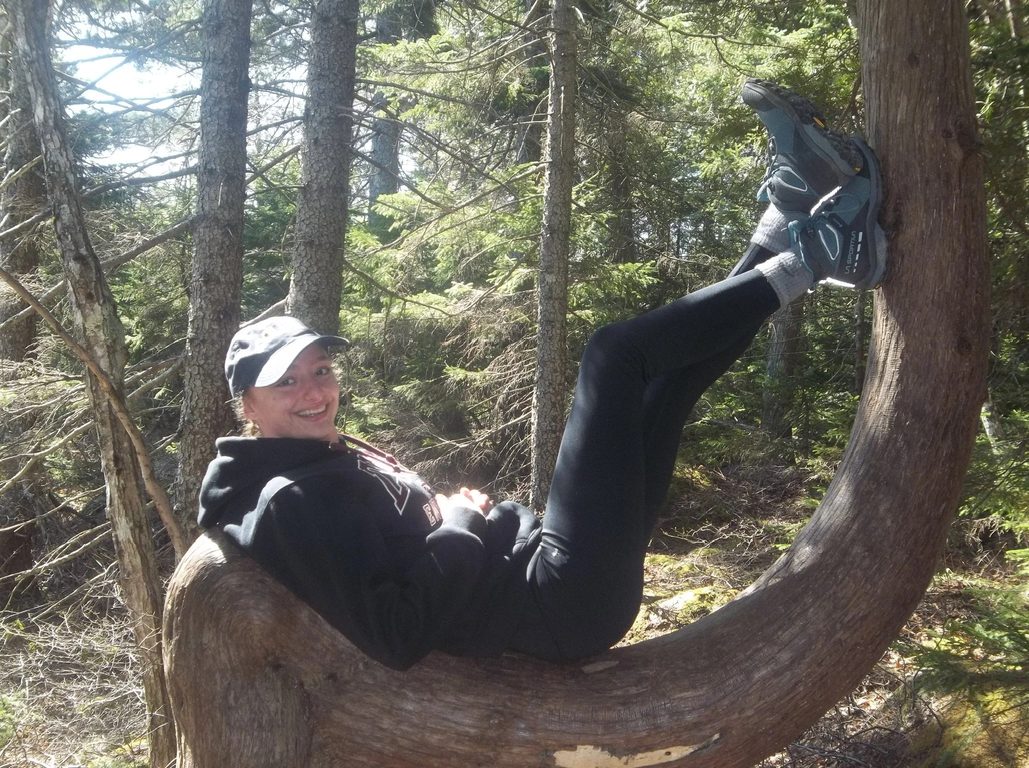 Young adult woman sitting on a curved tree branch.