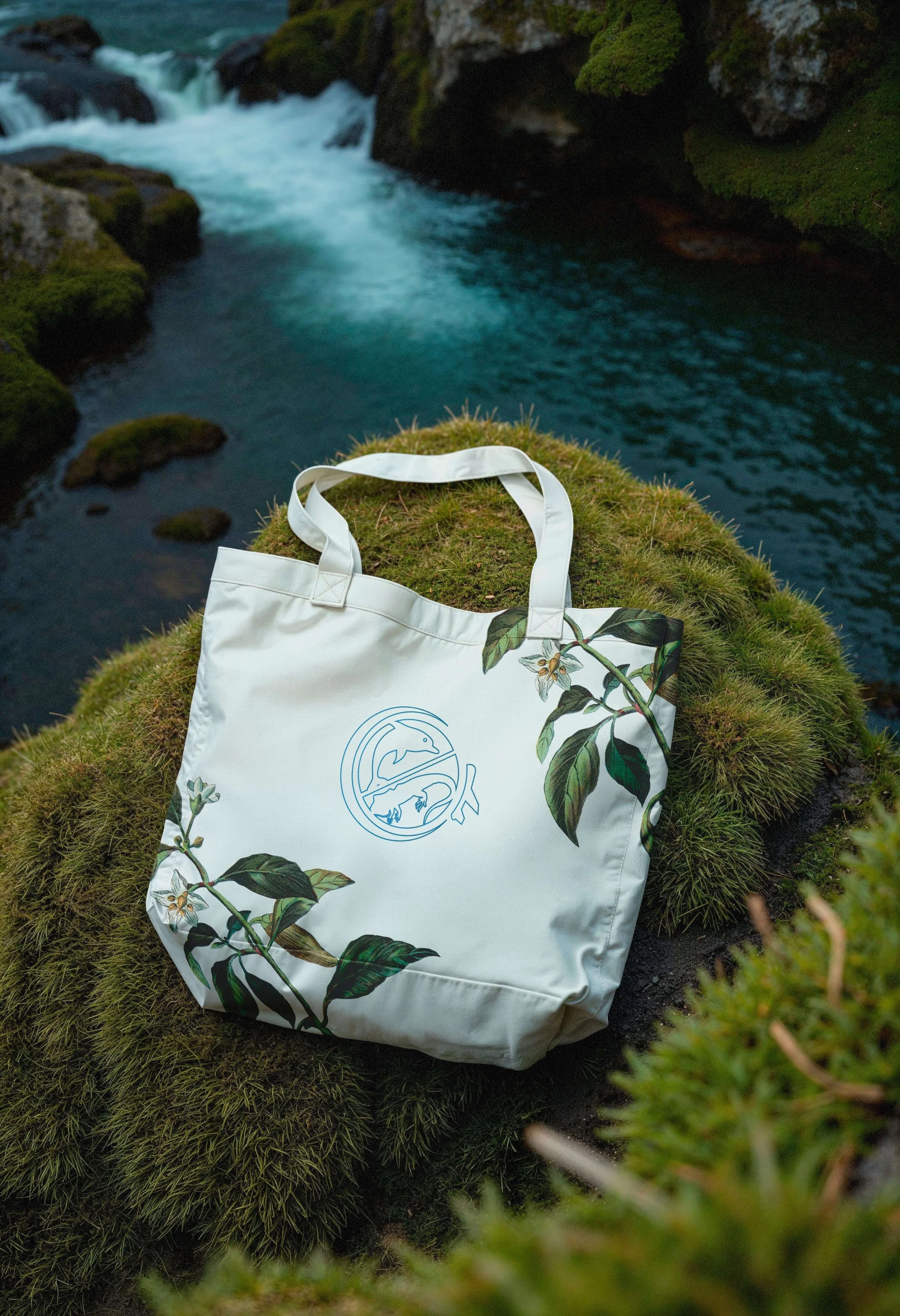 Branded tote bag with botanical illustration on mossy rock.