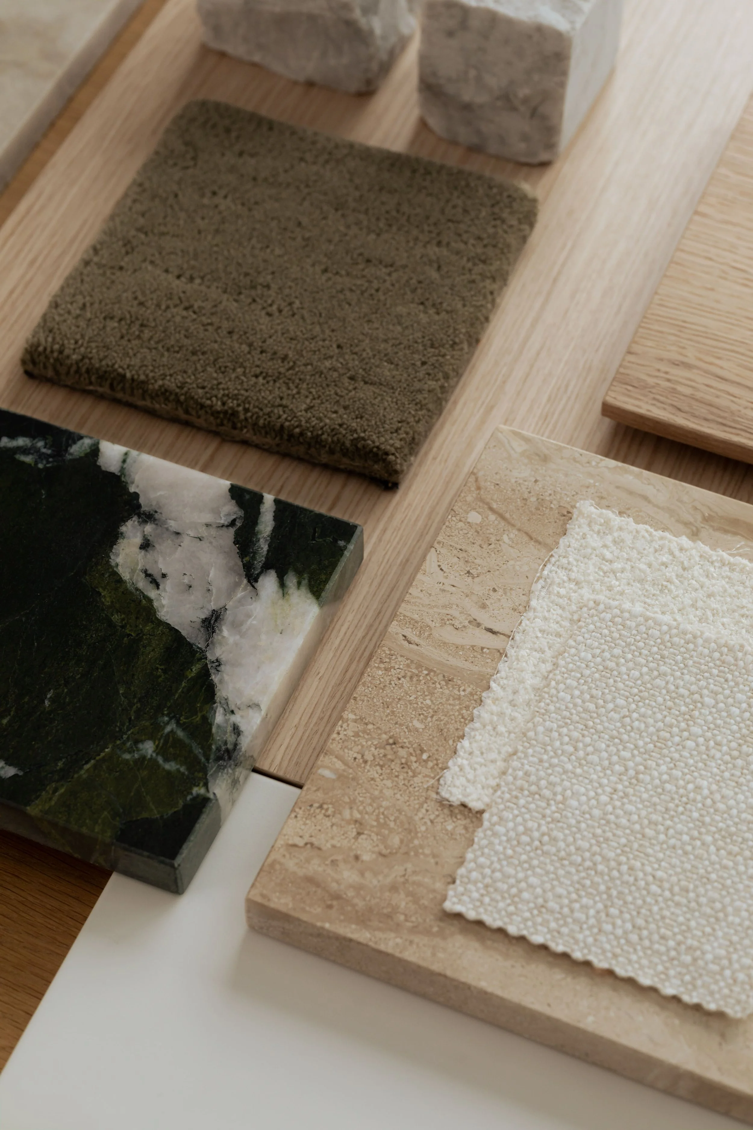 Interior material samples featuring green textile, marble, wood, and travertine.