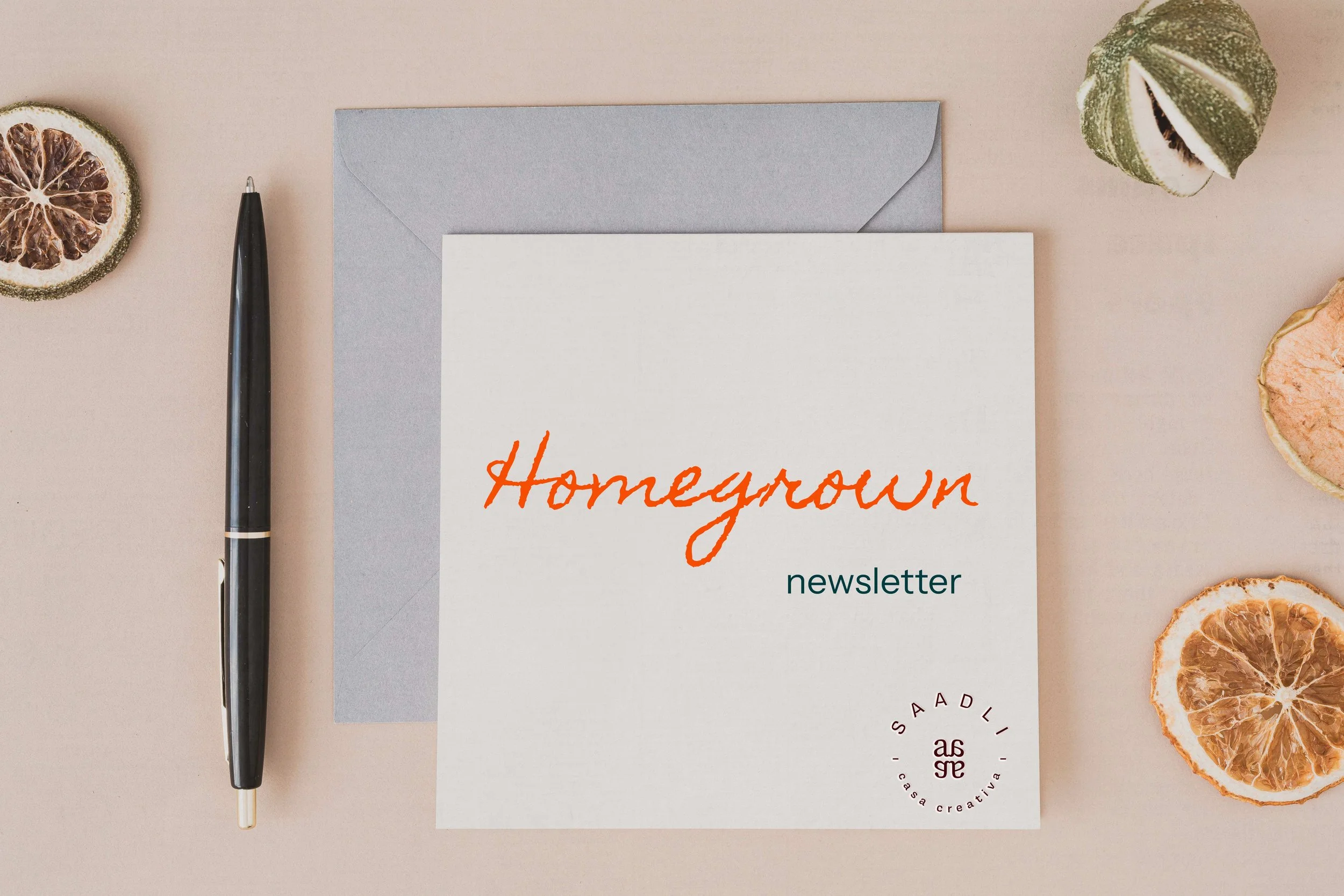 Homegrown newsletter card with a pen and dried citrus slices on a neutral background.