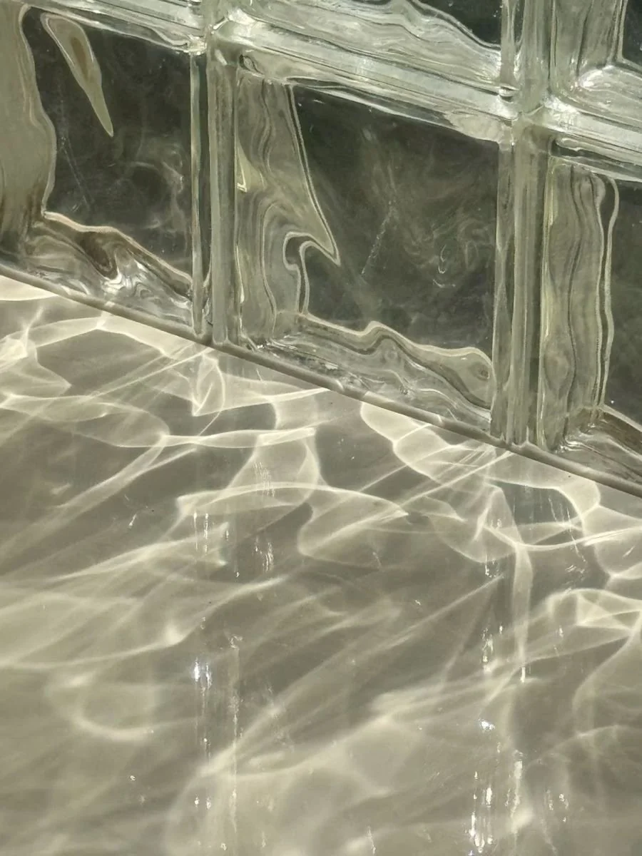 A still from the 2019 work *Natural Caustics*, showing the sun’s reflection and bright lines of light refracted through glass blocks on the floor of a swimming pool