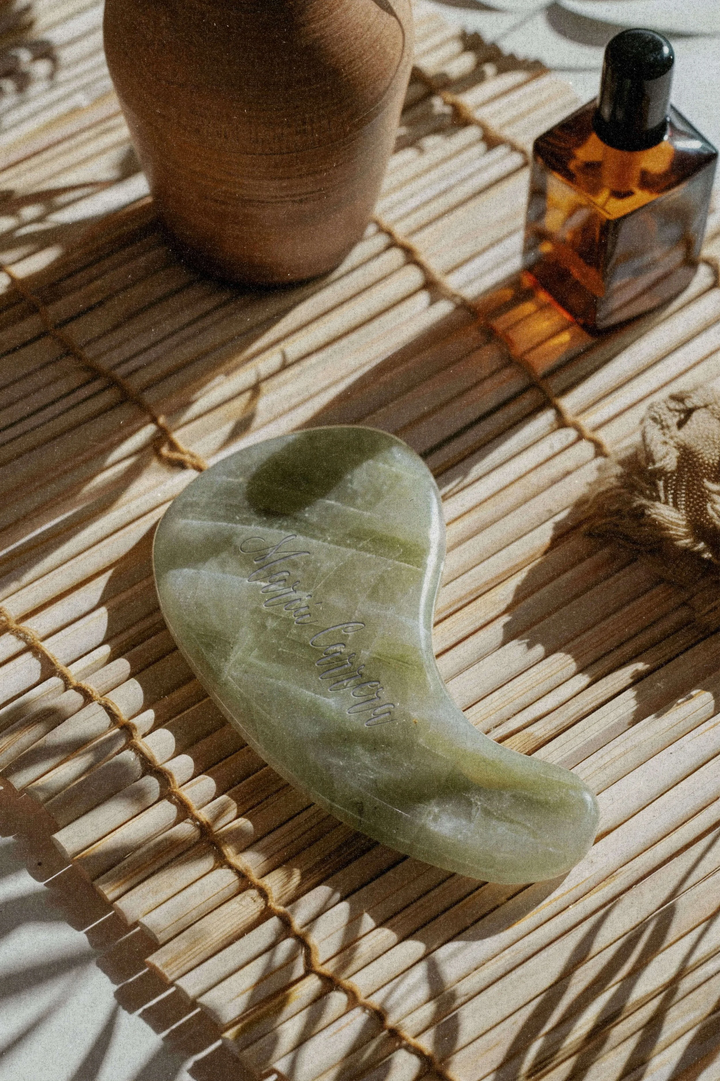 Green jade gua sha tool on a bamboo mat.