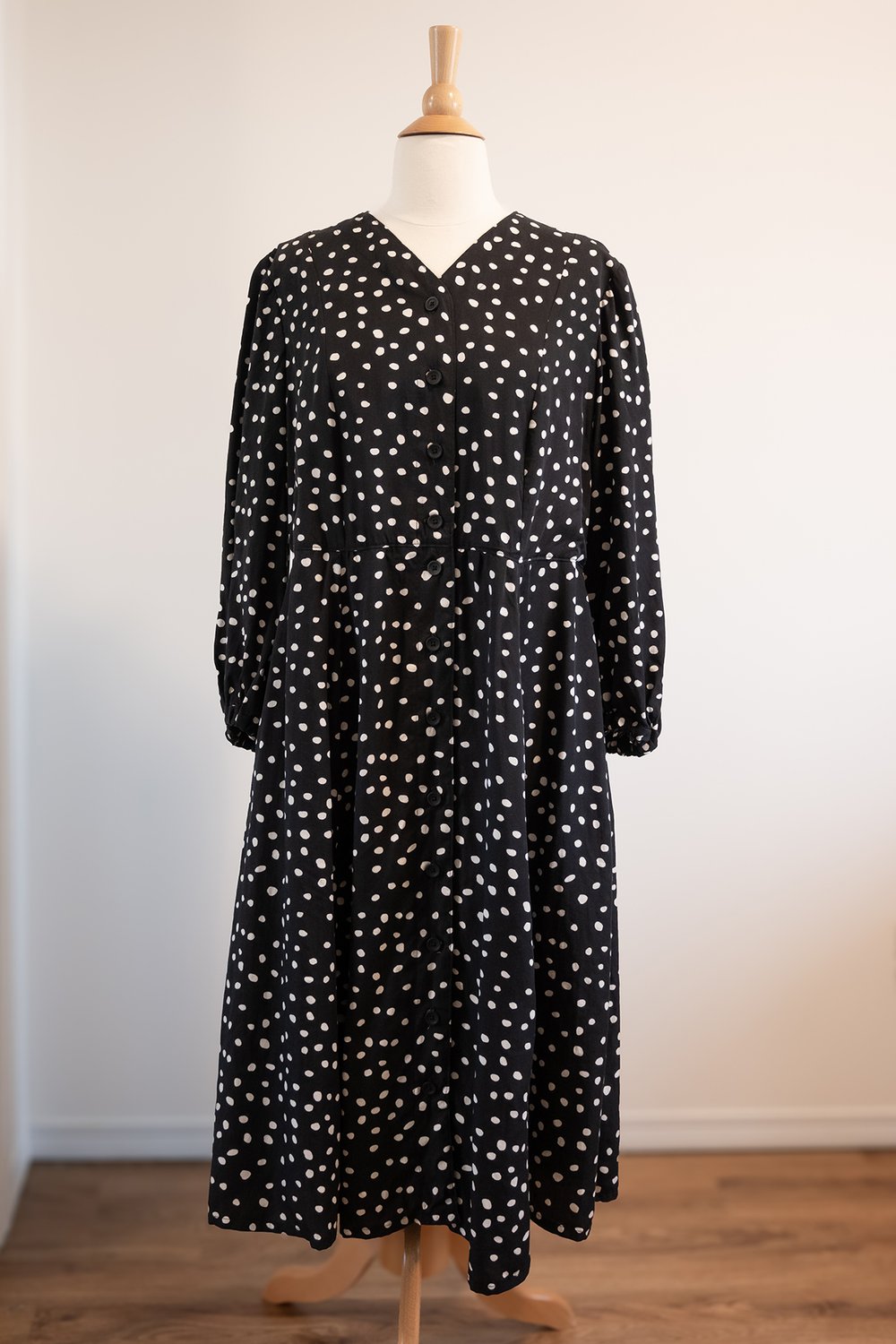 A black and white polka dot dress is on a dress form; the dress is made out of lyocell fabric and has a drape.