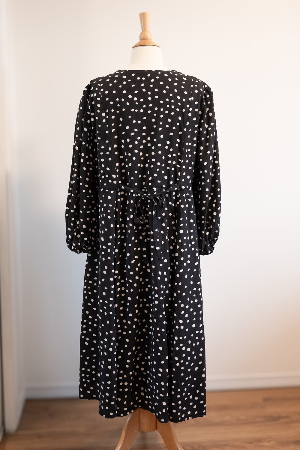 A black and white polka dot dress is on a dress form; the dress is made out of lyocell fabric and has a drape.