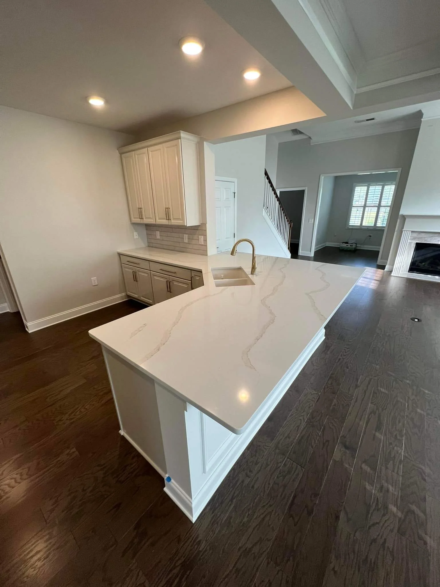Kitchen with white countertops, dark hardwood floors, and cream cabinets. Recessed lighting and a chimney fireplace are visible in the adjoining living area.