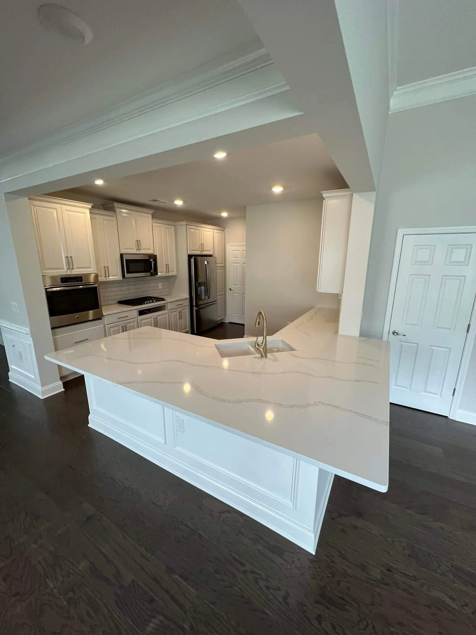 Modern kitchen with white cabinets, a light-colored marble island, stainless steel appliances, dark hardwood floors, and recessed lighting.