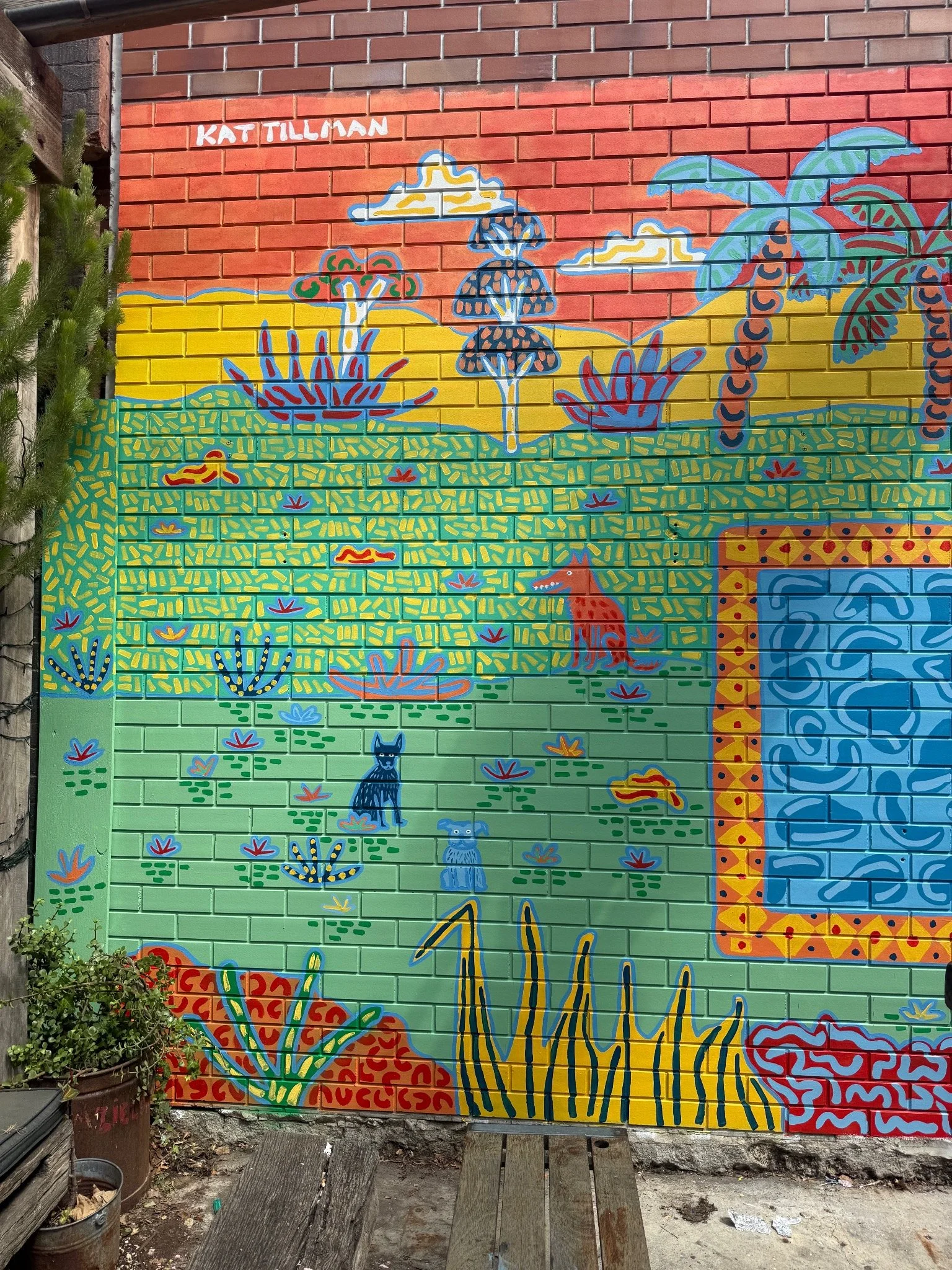 Close-up of Kat Tillman’s colourful brick mural featuring a hand-painted palm tree and bold patterned landscape.