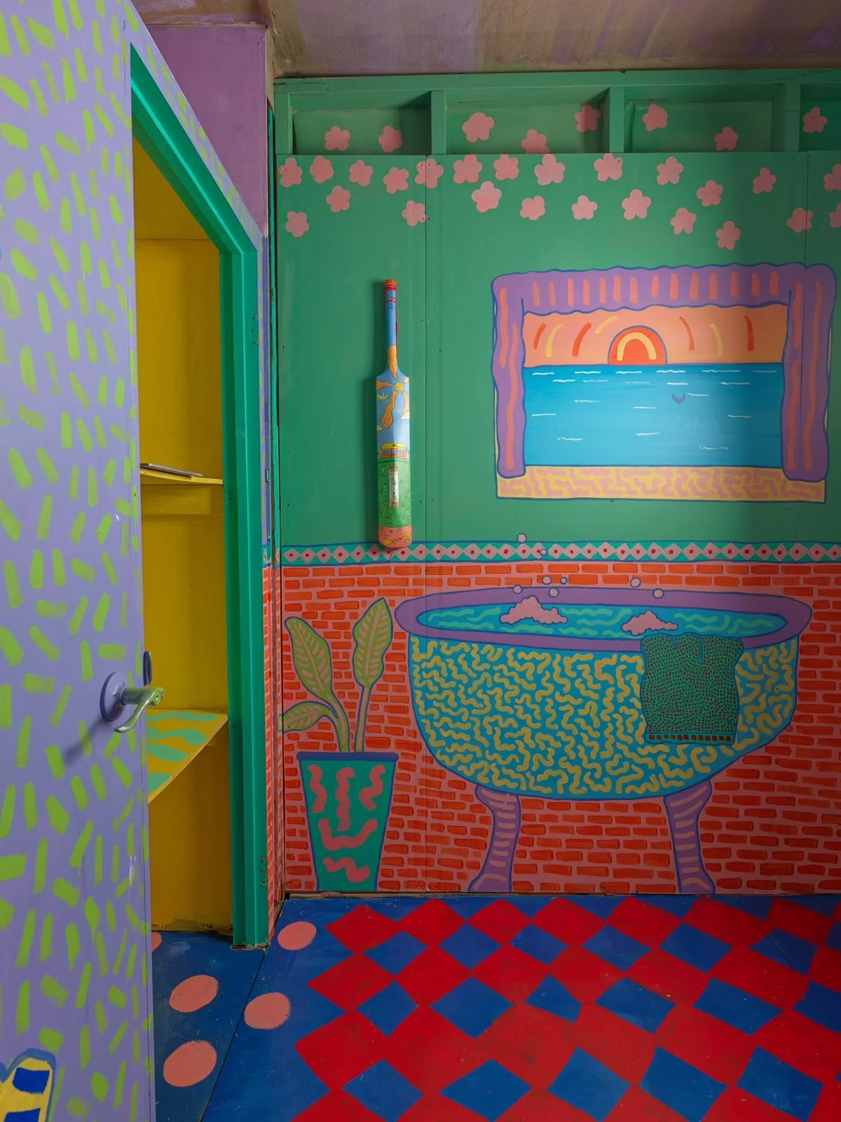 Brightly painted bathroom in the Side Quest Stories house, featuring turquoise walls, a pink-framed mirror, colourful patterned tiles and bold decorative illustrations.