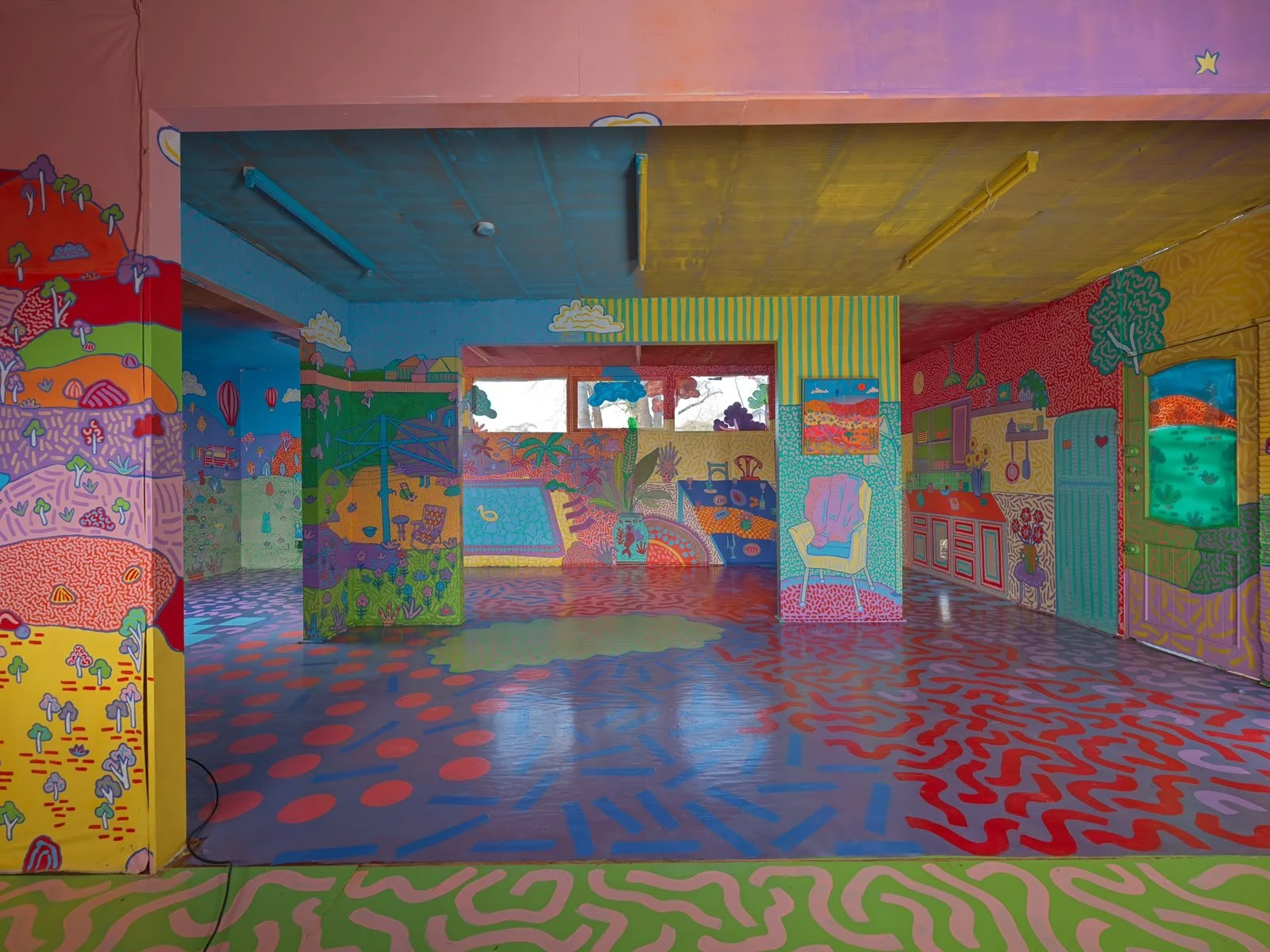 Immersive mural installation inside the Side Quest Stories house, featuring brightly painted walls, ceilings and floors with bold colours, whimsical landscapes and geometric patterns.