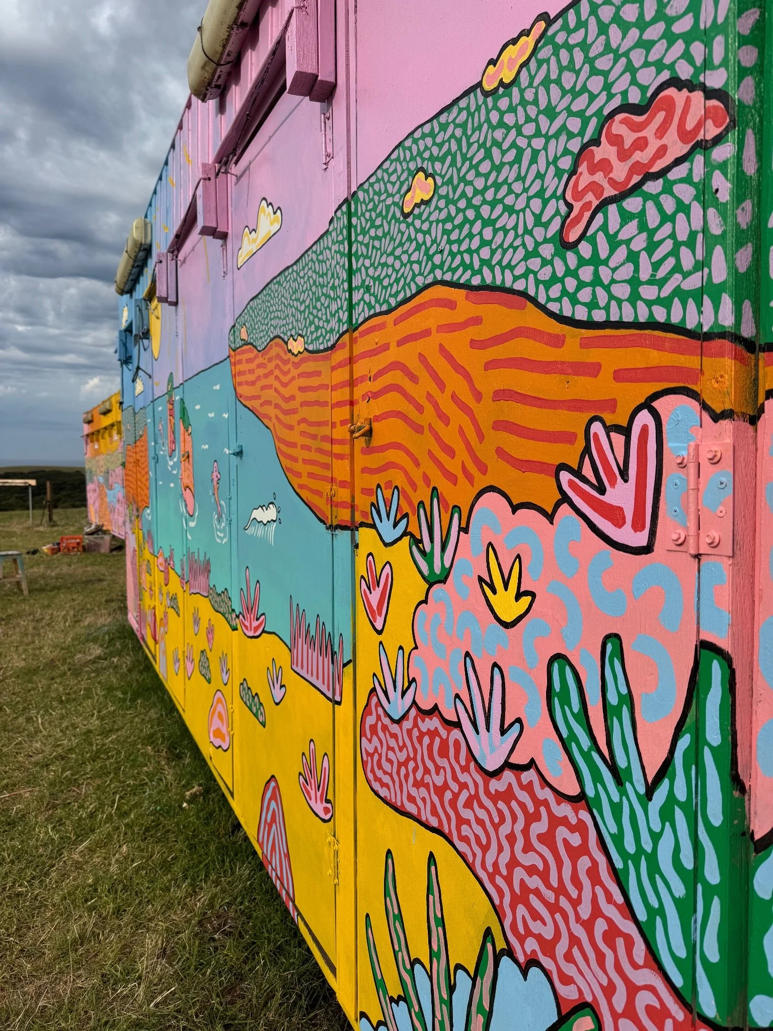Close-up of a colourful hand-painted festival mural by Australian artist Kat Tillman, featuring abstract native landscape forms in pink, green, orange and blue.