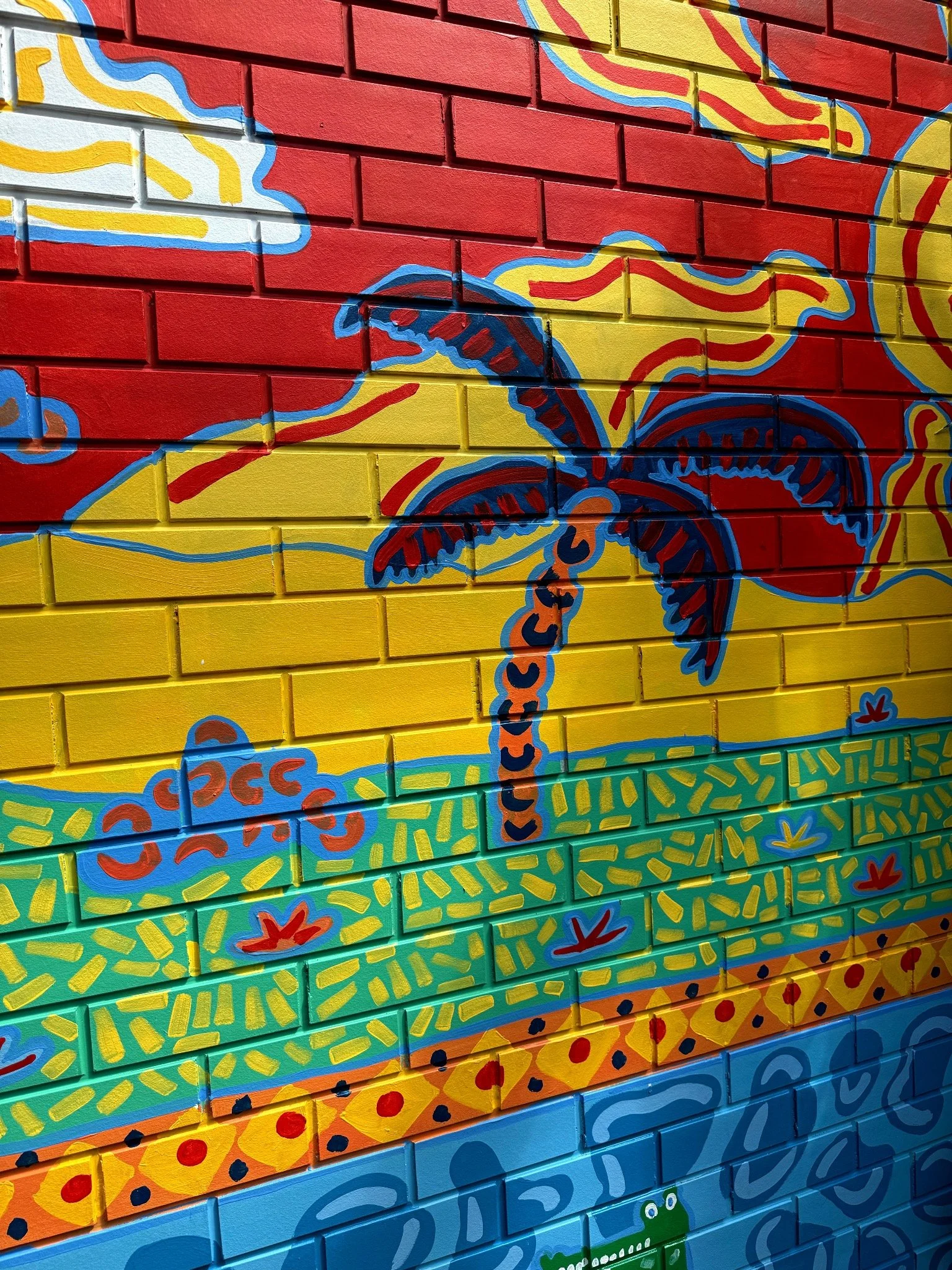 Close-up of Kat Tillman’s colourful brick mural featuring a hand-painted palm tree and bold patterned landscape.