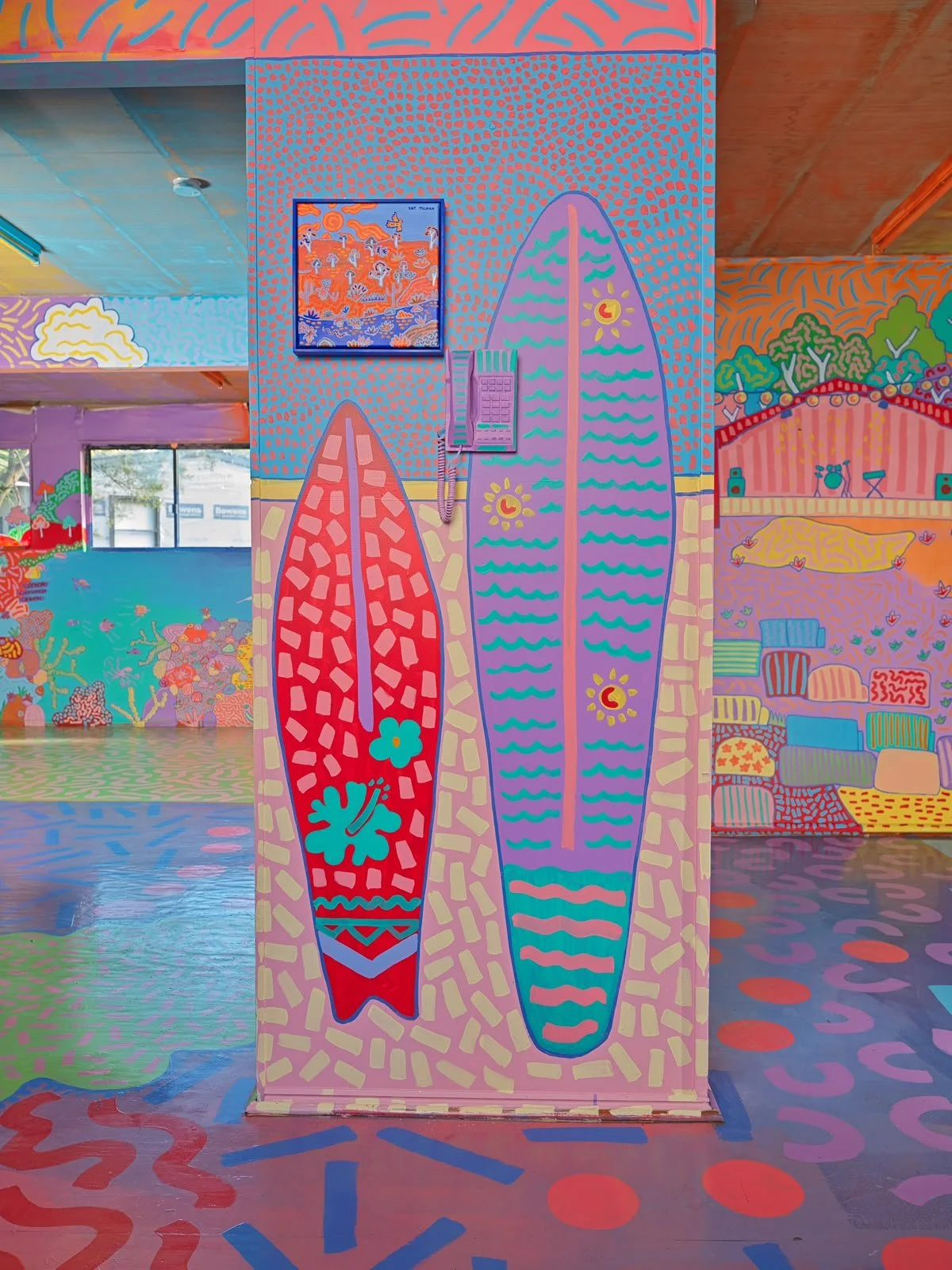 Colourful hand-painted surfboards displayed inside the Side Quest Stories house, surrounded by vibrant murals, playful patterns and illustrated landscapes.