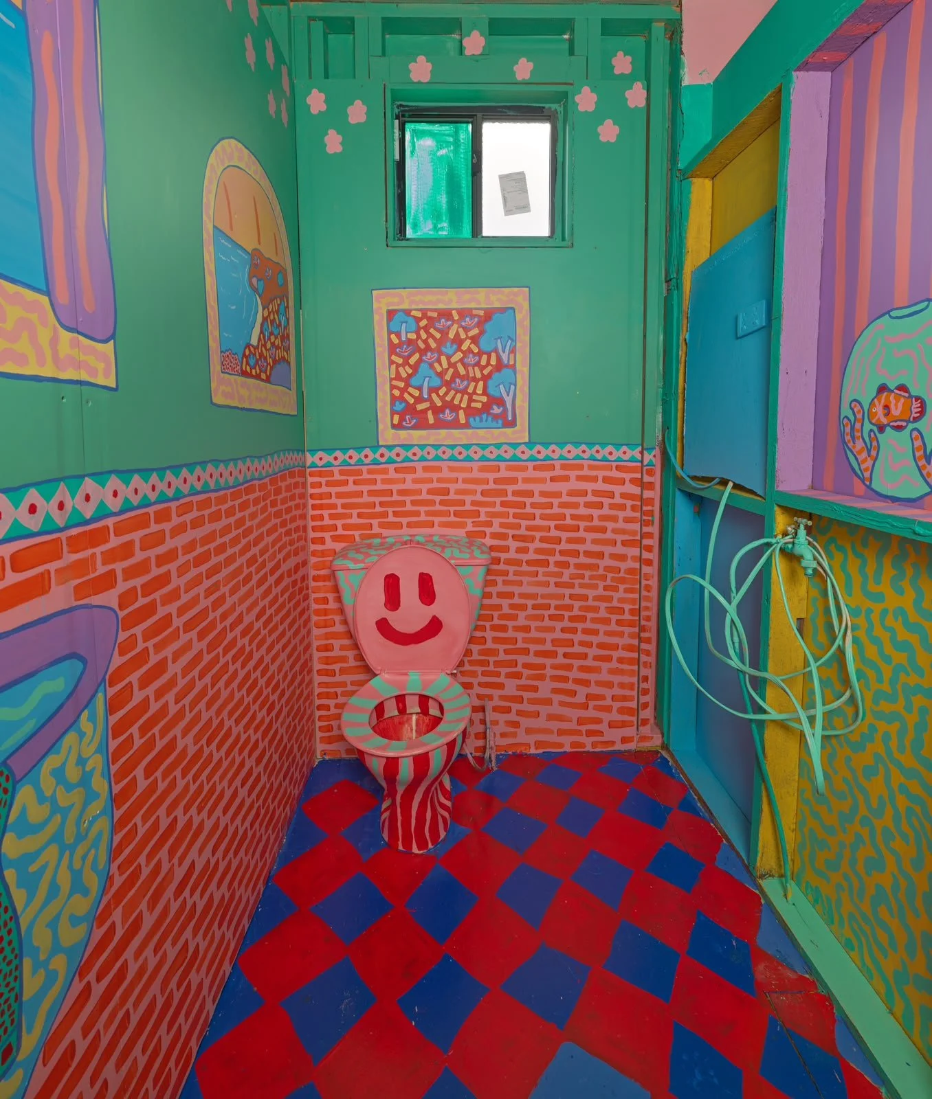 Playful bathroom mural by Kat Tillman featuring turquoise walls, bright red and blue checkerboard flooring, colourful illustrations and a smiling character.
