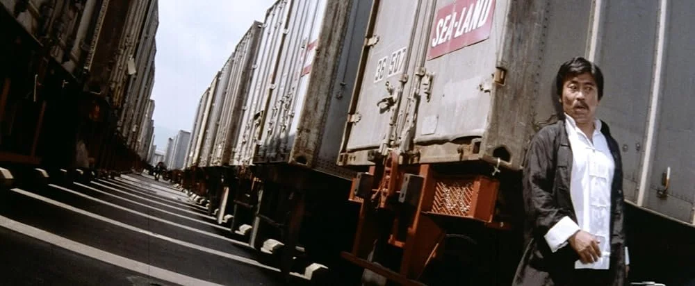 A man stands beside a row of freight cars in Bruce and the Iron Finger (1979).