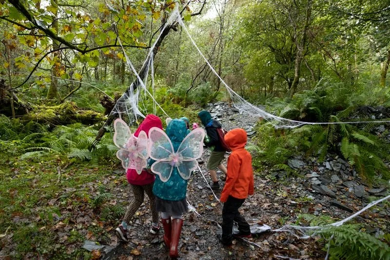 Children exploring a forest trail with fairy wings costumes and spider webs.