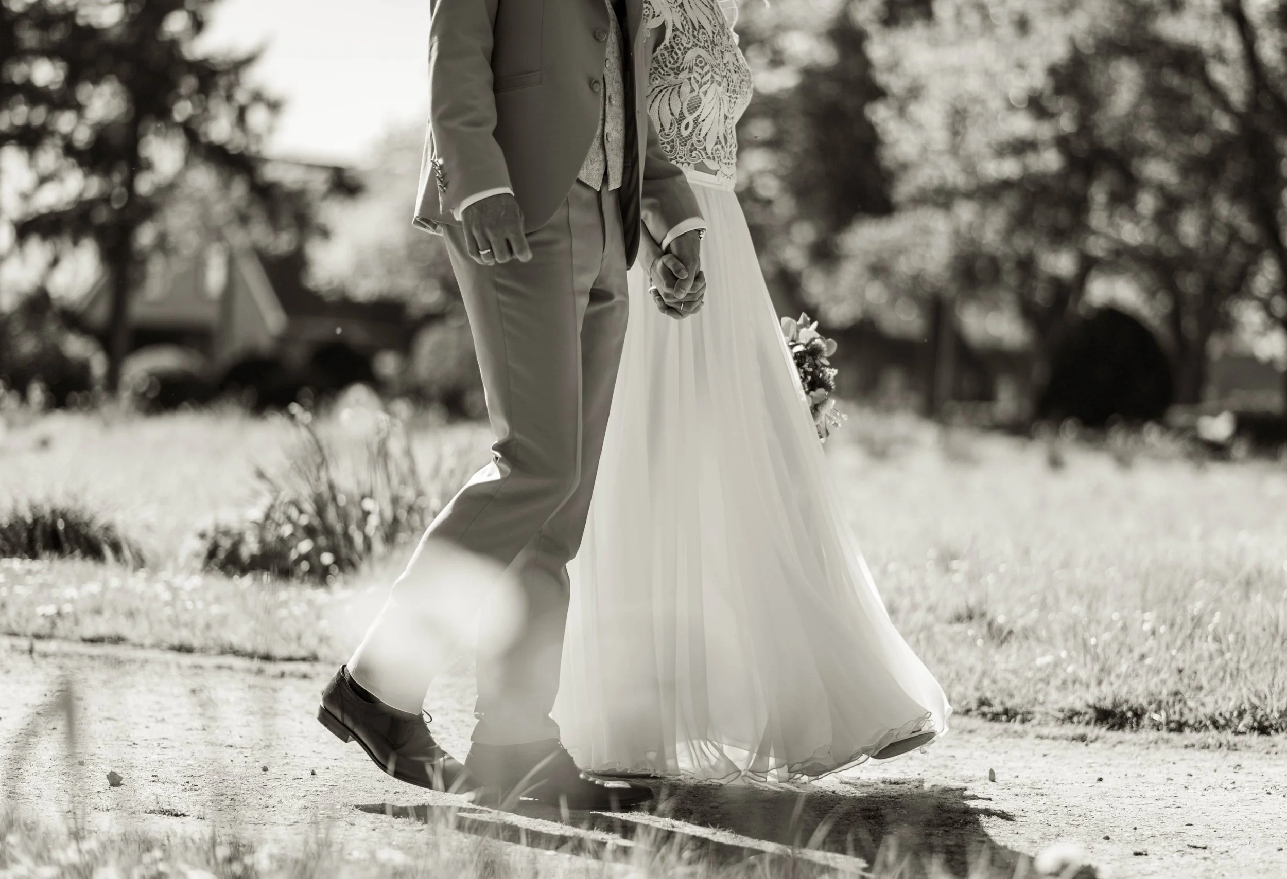 Schwarzweiß Hochzeitsfoto – Braut und Bräutigam halten Hände beim Spaziergang