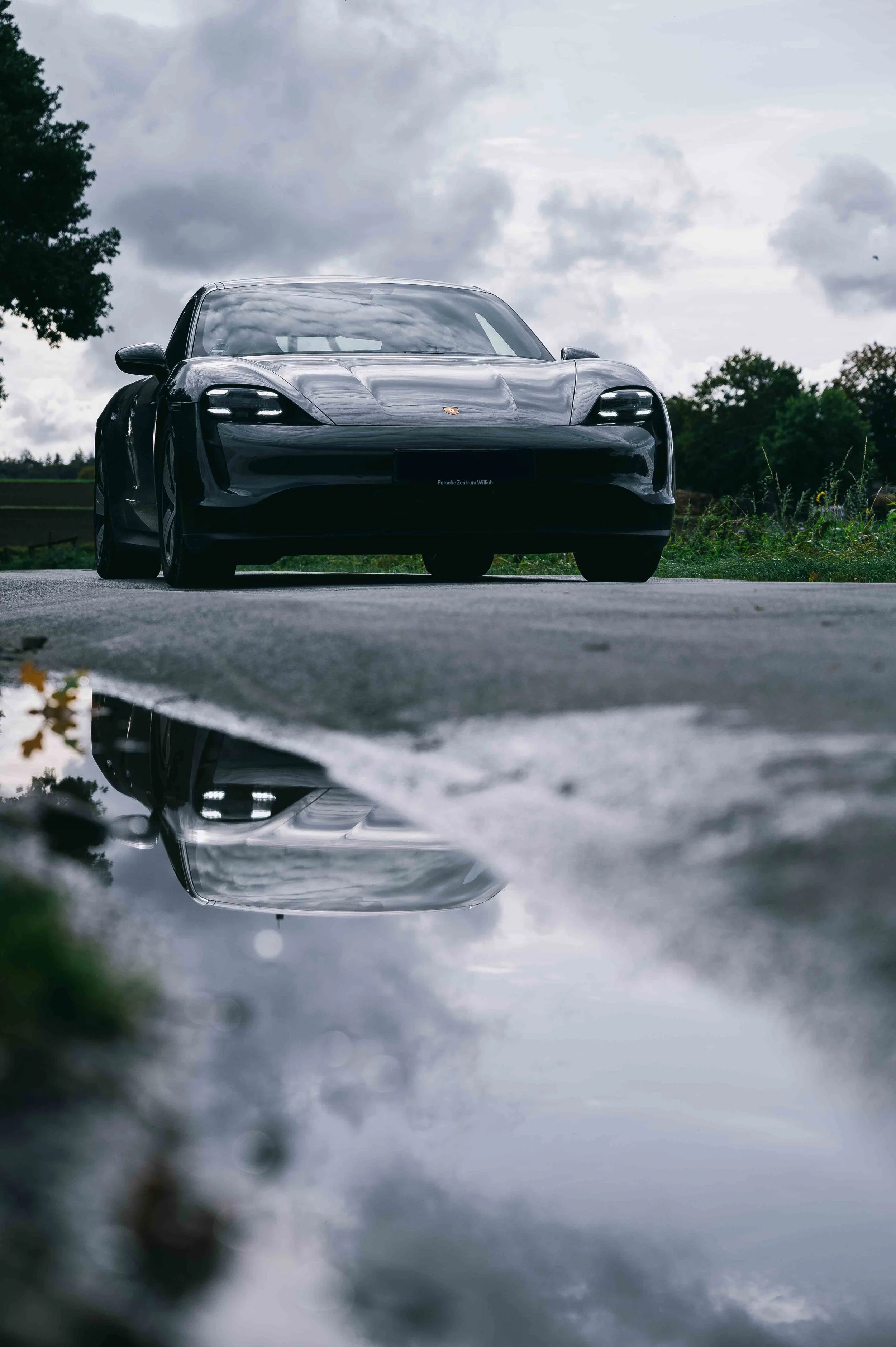 Ein Porsche Taycan 4S spiegelt sich in Pfütze auf Landstraße
