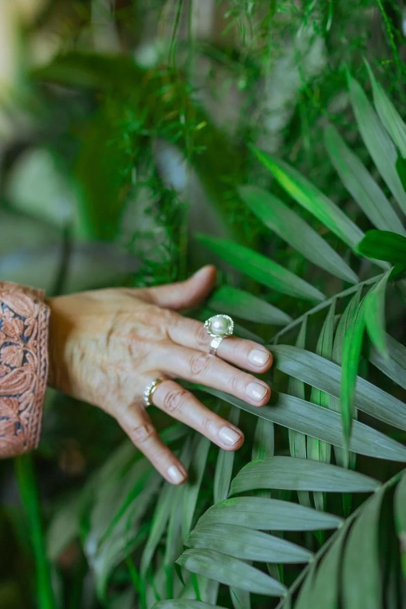 Close-up of a postmenopausal woman's hand with rings, resting on green leaves in a lush garden.
