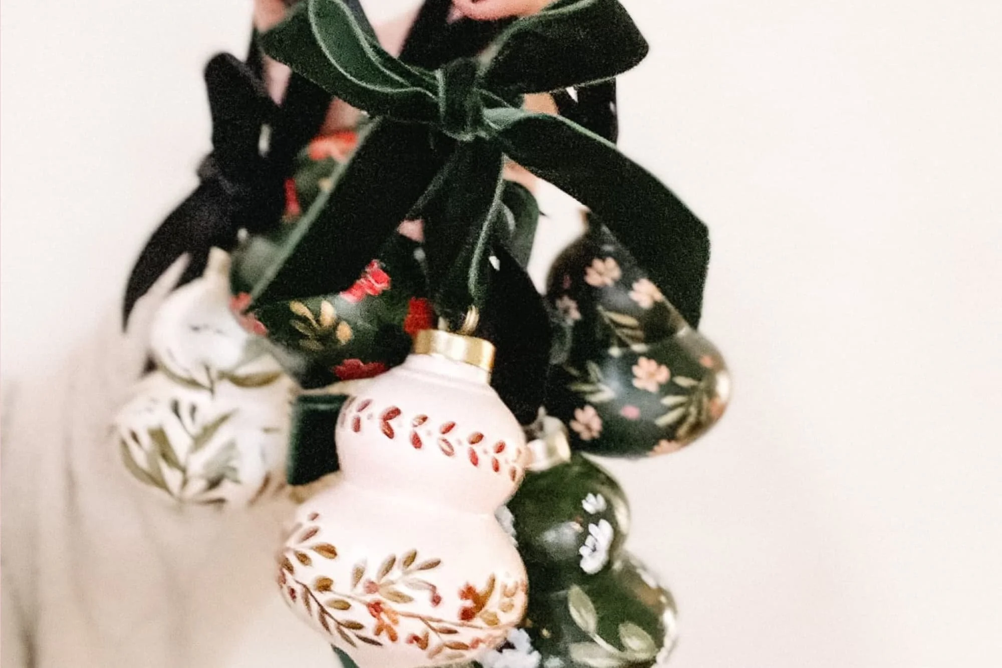 Several hand-painted heirloom Christmas ornaments in different painted floral designs, each hung with a velvet ribbon