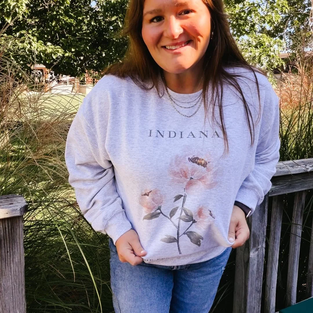 Woman on a deck wearing the Pink Peony Indiana watercolor sweatshirt