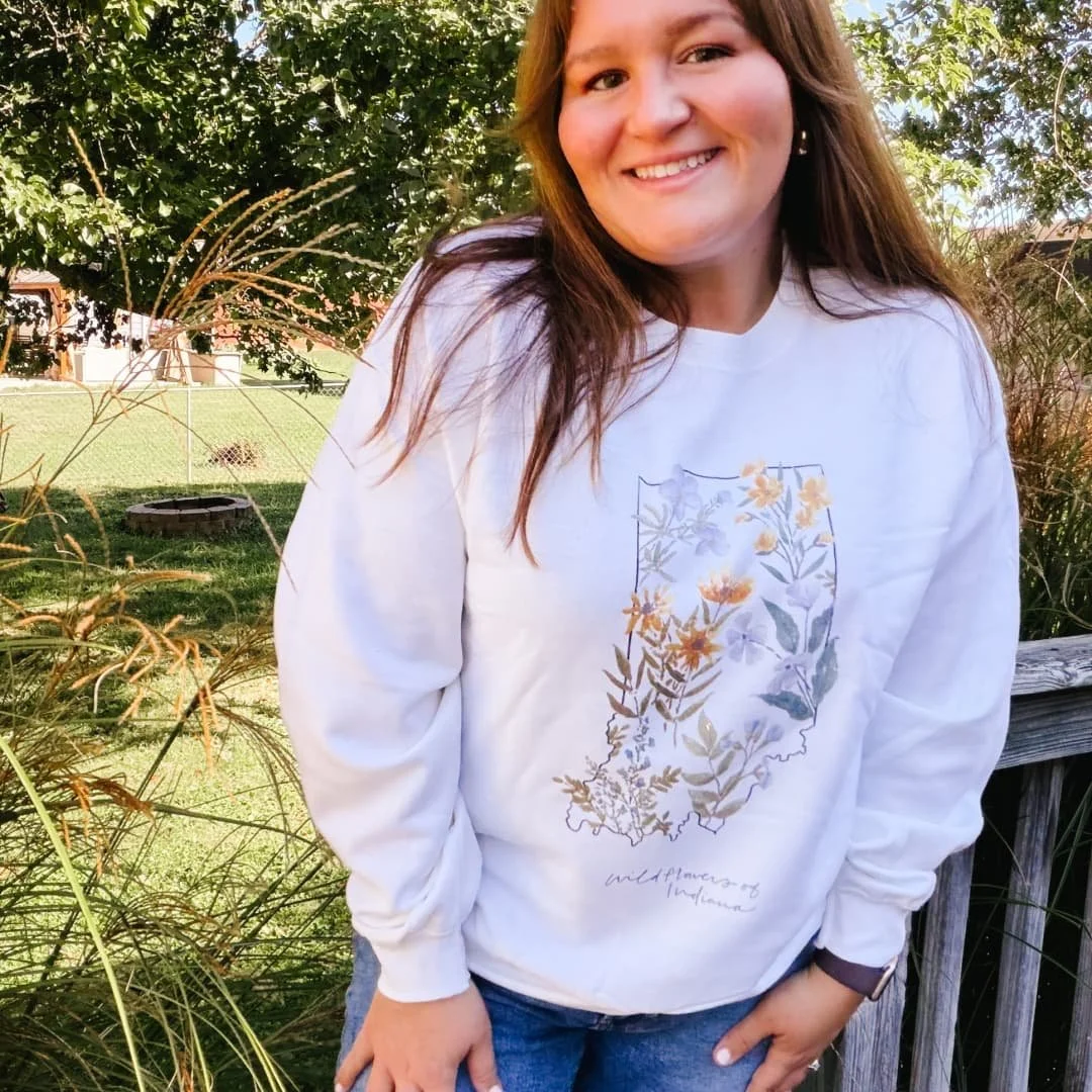 Woman on a deck wearing the State of Indiana Wildflowers watercolor sweatshirt