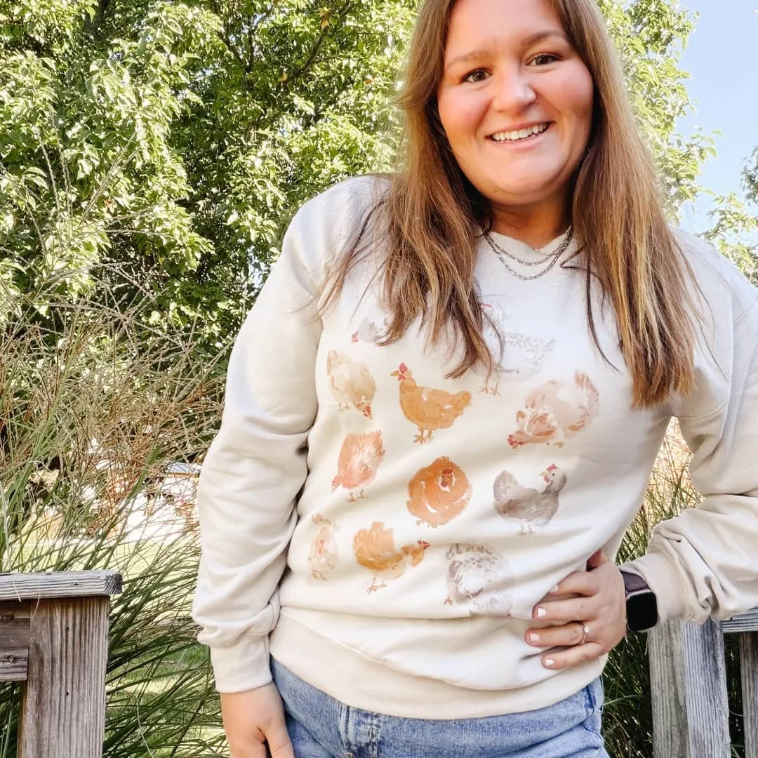 Woman on a deck wearing the Chickens farmhouse watercolor sweatshirt
