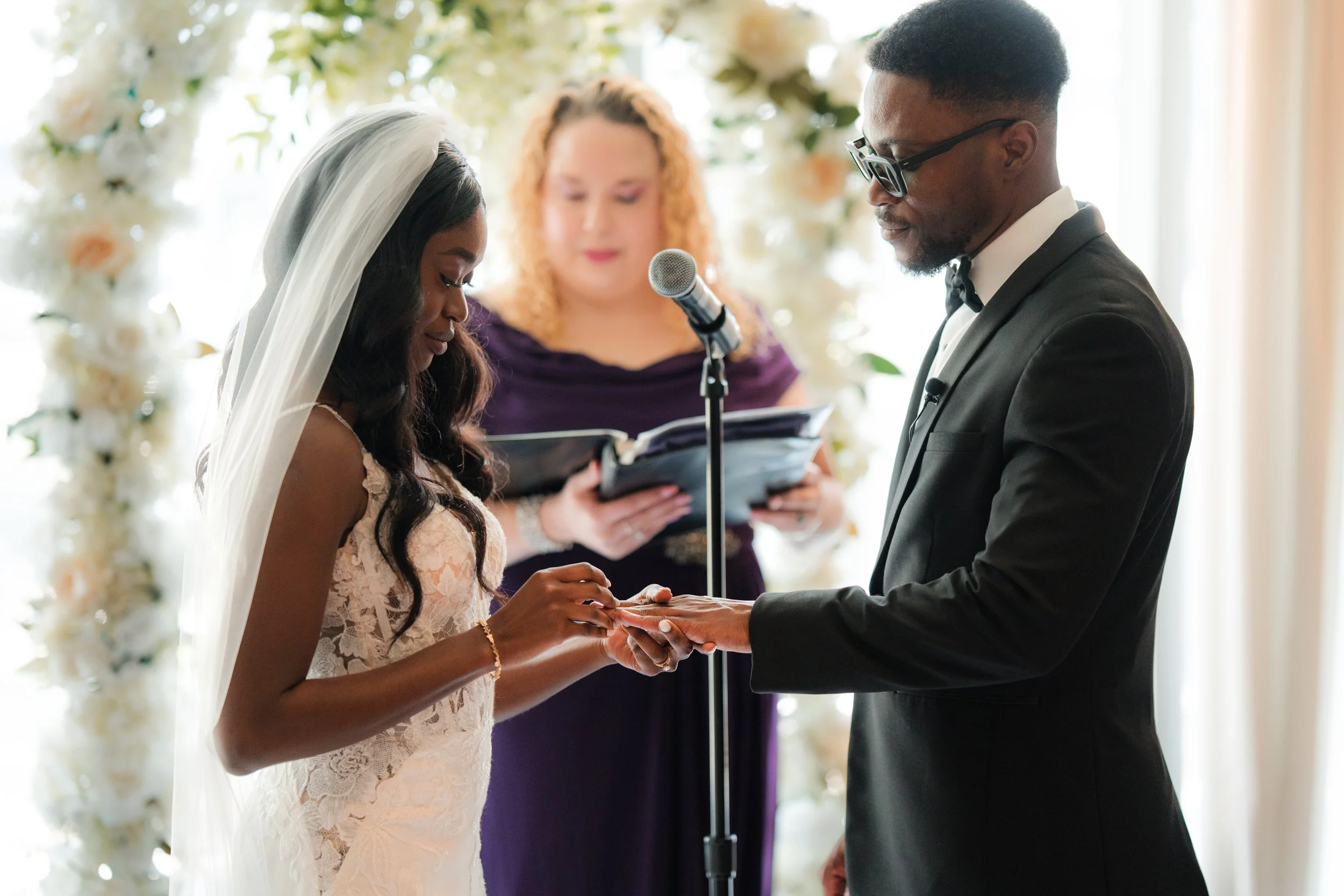 Couple exchanging rings during RPM Seafood Micro Wedding with professional officiant and white floral arch