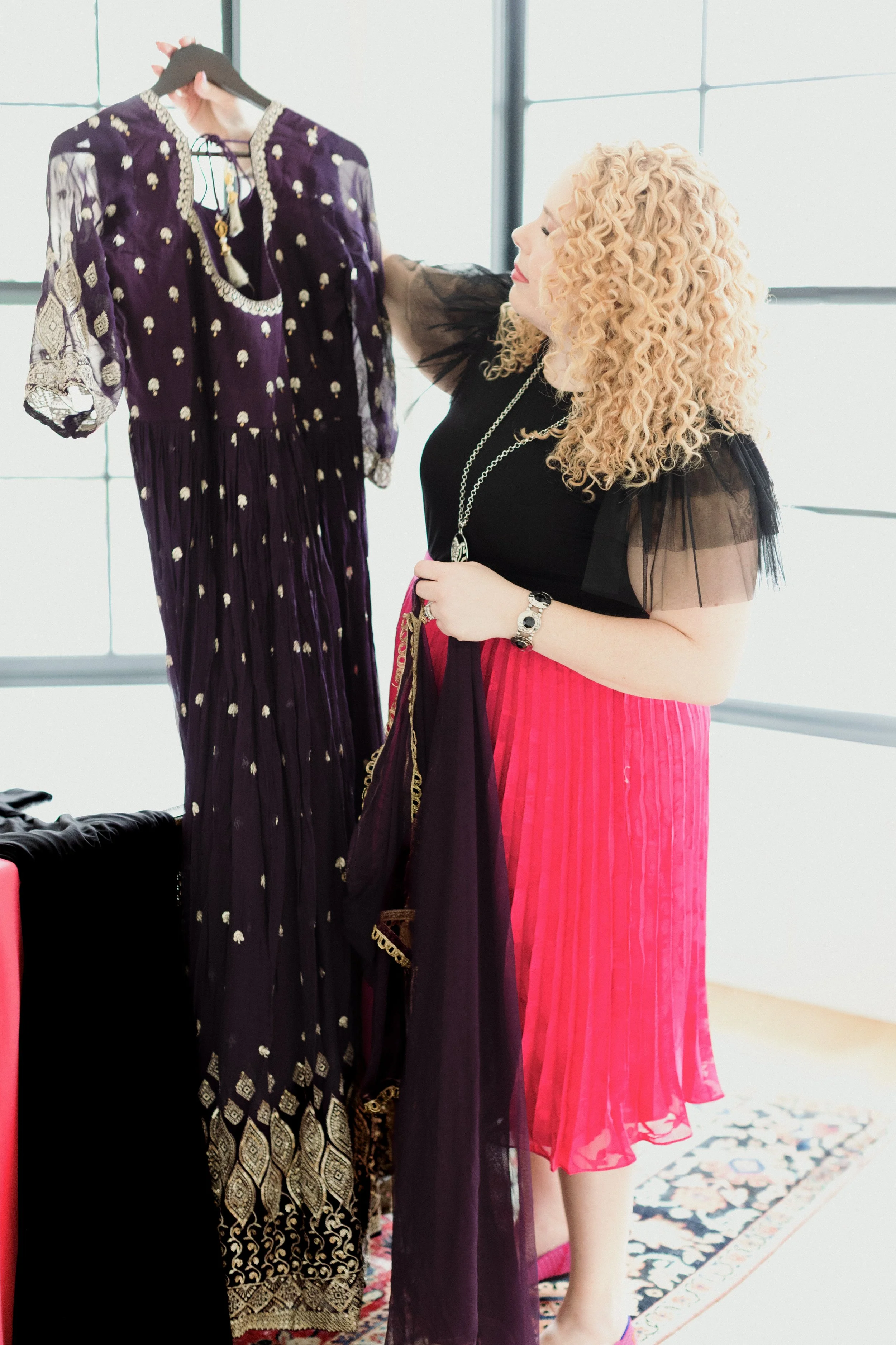 Chicago wedding officiant Carla Doshi choosing the perfect outfit for her upcoming wedding.  Holding a purple Indian Kurta and a black dress.