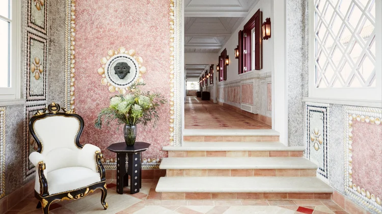 Hallway with pink shell-encrusted walls, a vase of flowers, and an ornate black and white armchair - christian Louboutin villas