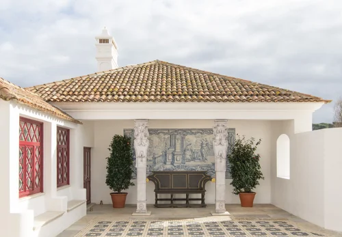 Exterior courtyard with a tiled roof, decorative azulejo panel, and potted plants flanking a stone bench - christian Louboutin villas