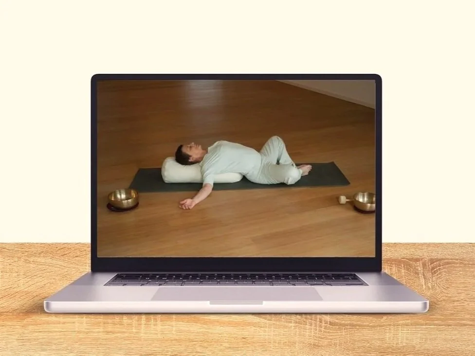 Yogalehrerin zeigt Asana auf Matte. davor Klangschalen. Auf Monitor eines Laptops zu sehen.