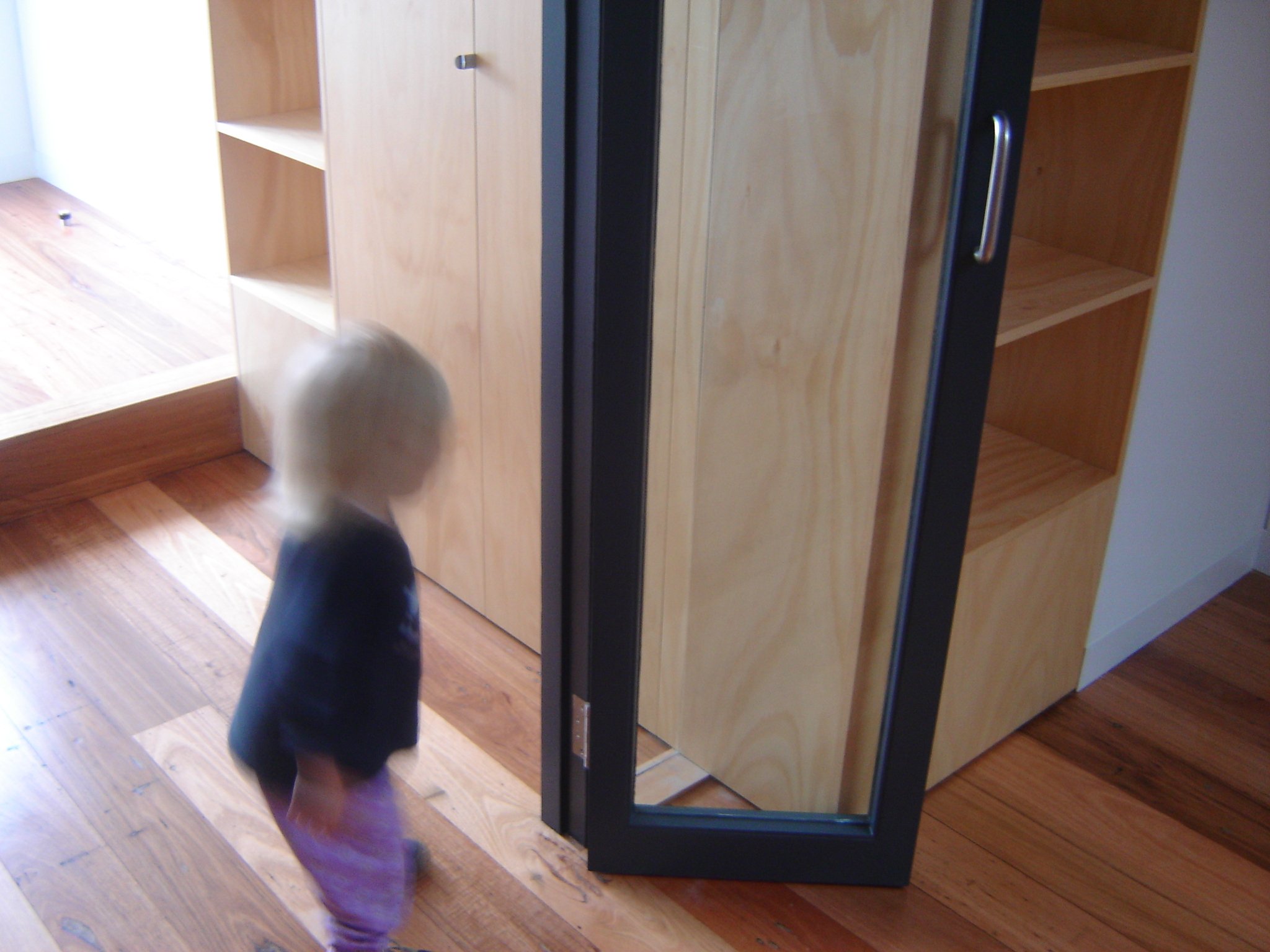  Built-in joinery shapes attic rooms with wardrobe, shelving, and kitchenette defining functional zones in compact space.  