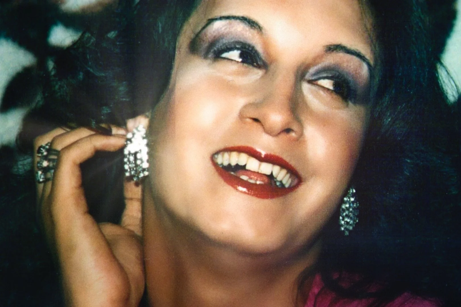 Georgina Beyers, looking youthful and glamorous. Red lipstick, glittering earrings, huge smile.