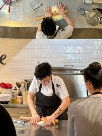 A photo of tutor Aeisha Ali-Khodja rolling out pastry in front of a class, reflected in a mirror above them